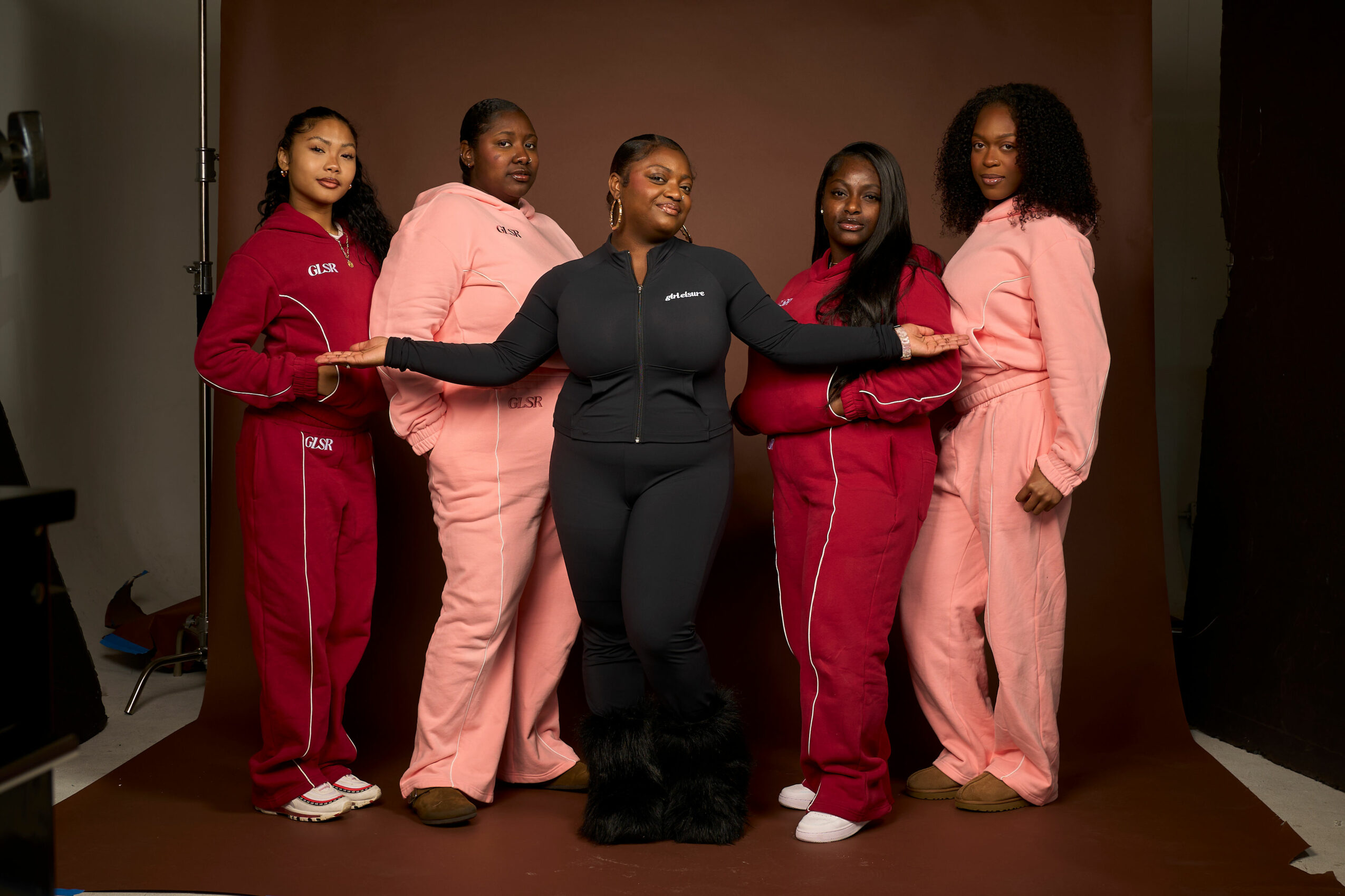 Five women in matching tracksuits pose together in a studio with a plain background.