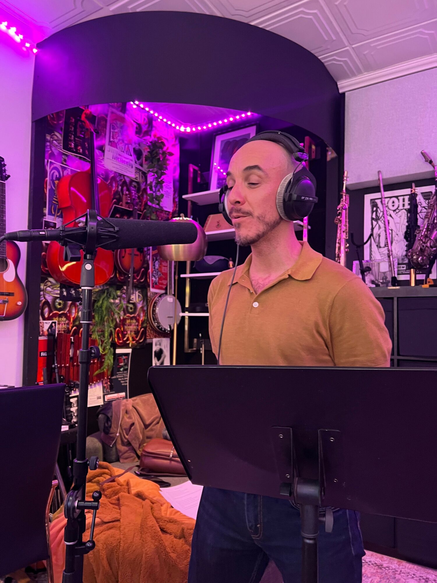 Man with headphones singing into microphone in a music studio with colorful wall decorations.