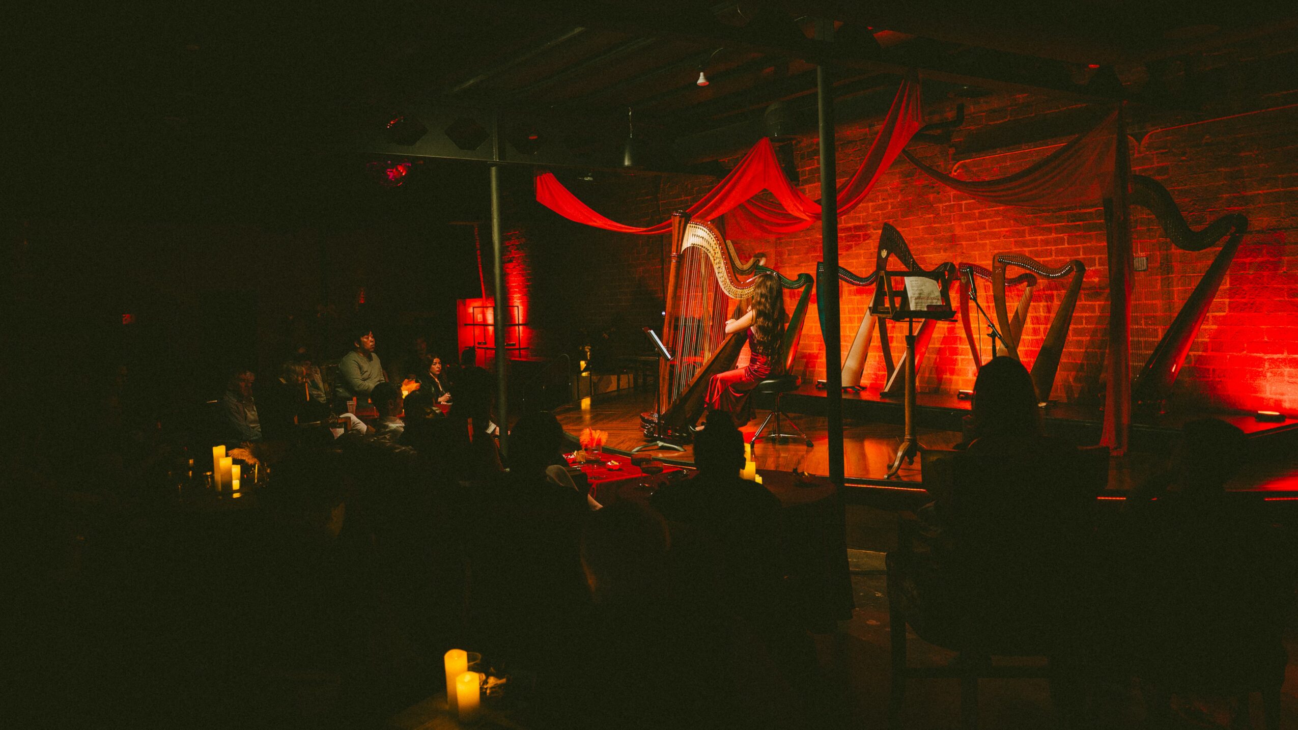 Stage with performer, red lighting, and audience in a dark venue with candles.
