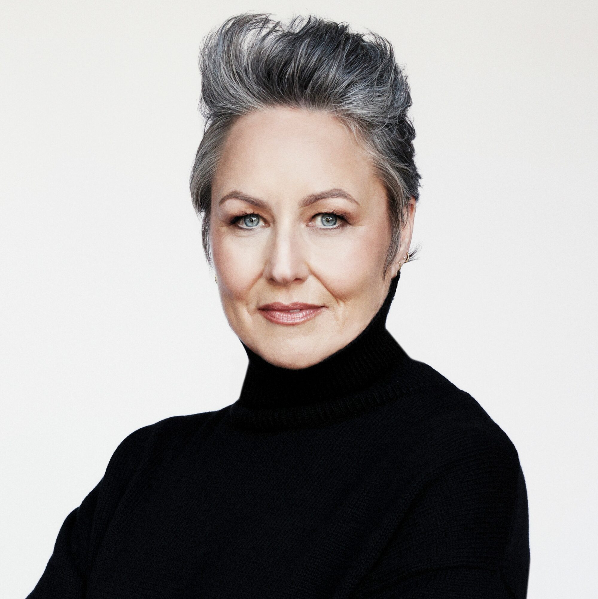 Woman with short gray hair and blue eyes wearing a black turtleneck, looking at the camera.