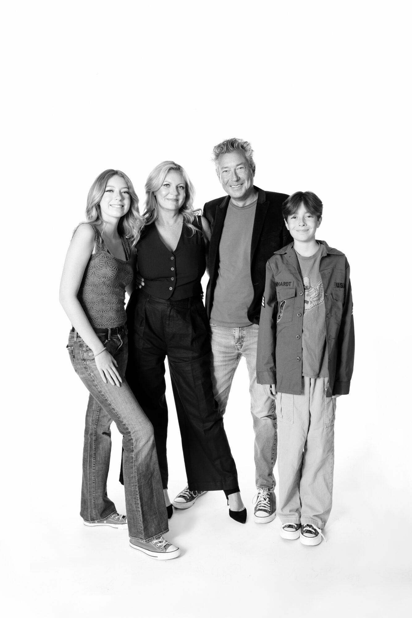 Four people standing together, smiling, in casual clothing, against a plain white background.