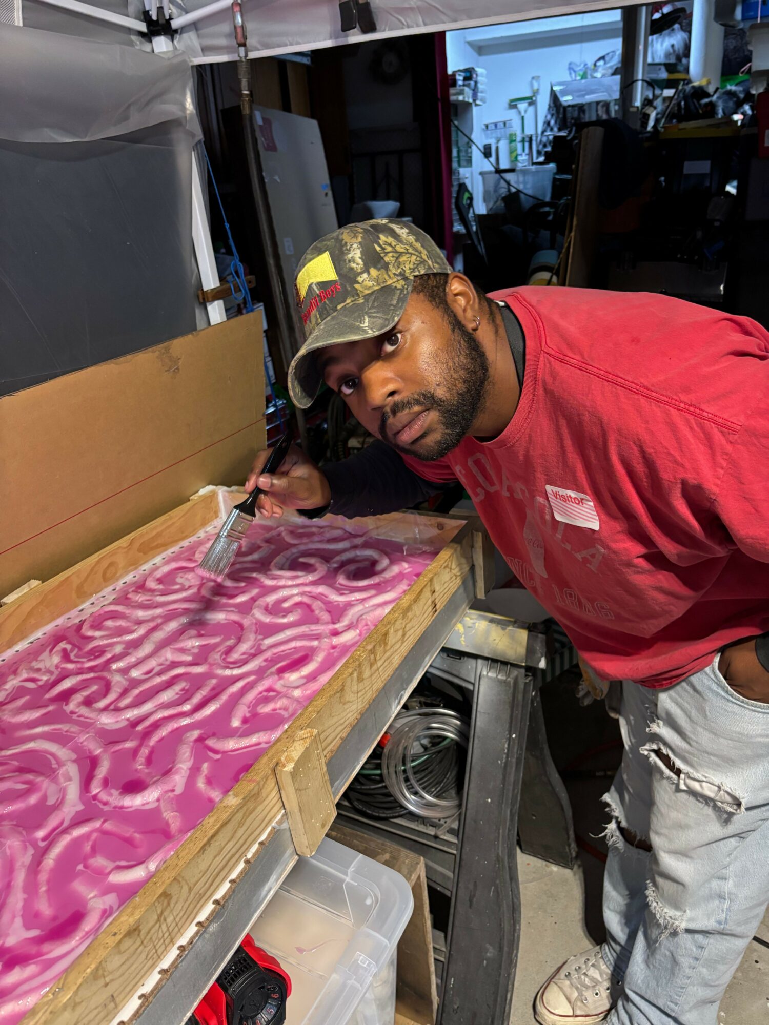 Man with a cap and glasses leaning over a pink and white patterned surface in a workshop.