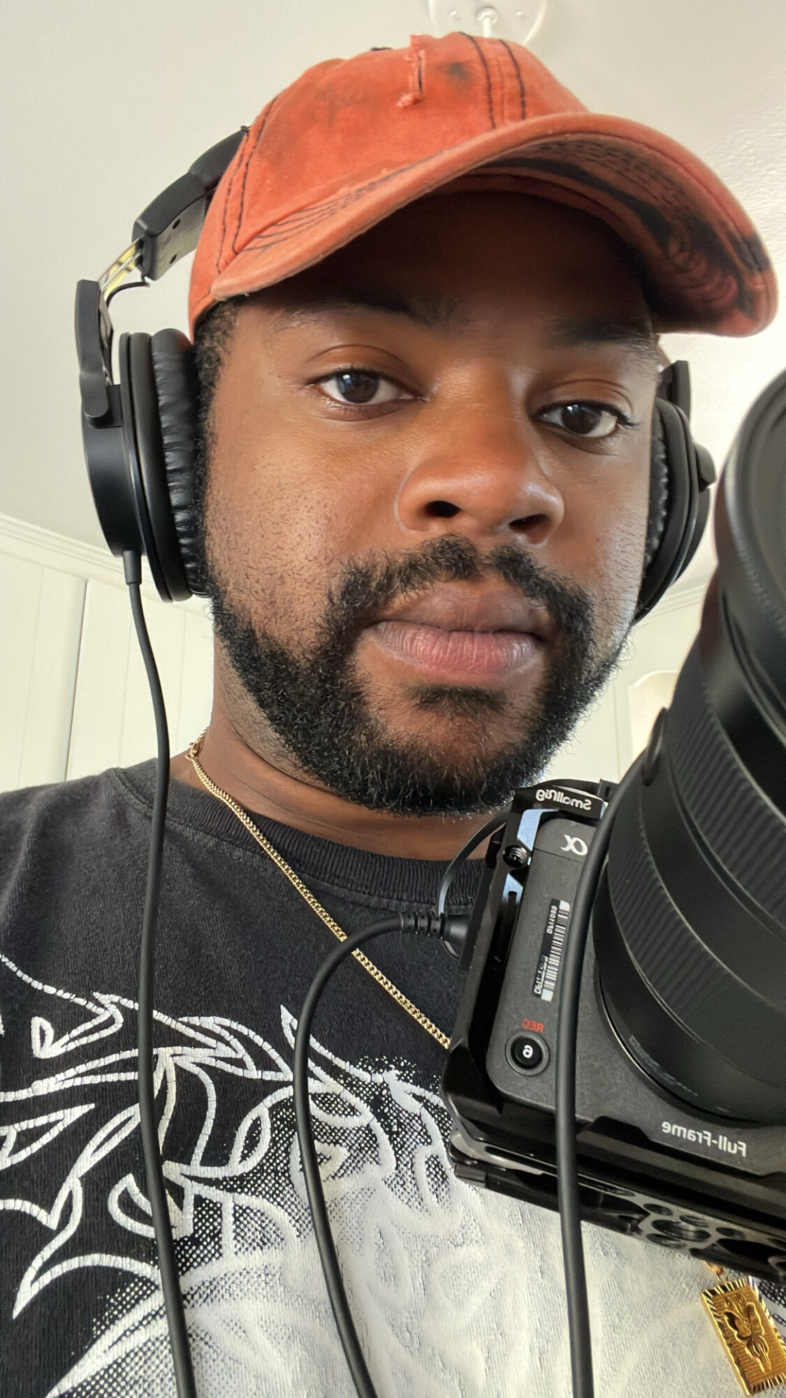 Person wearing a red cap and headphones, holding a camera, with a neutral background.