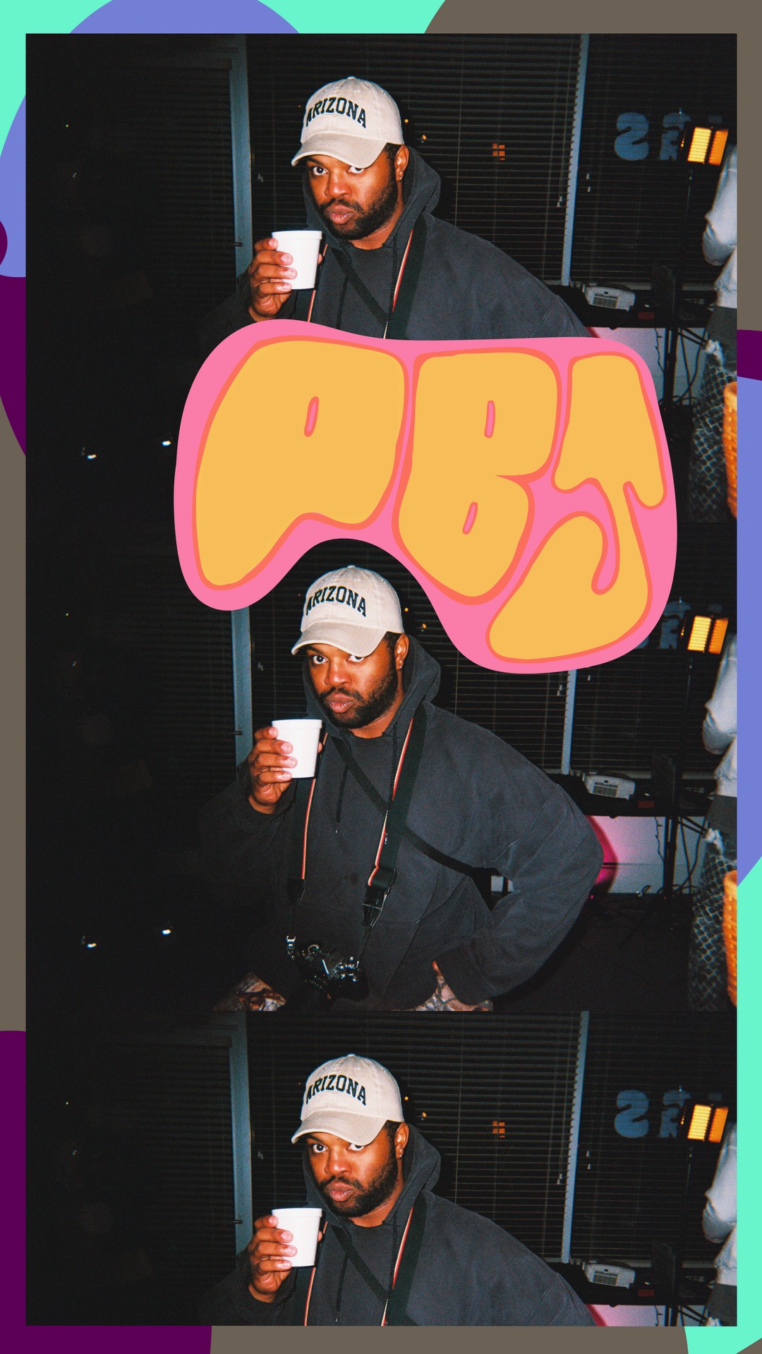 Man wearing a cap and glasses holding a drink, standing in front of sound equipment, with a large pink and yellow sign.