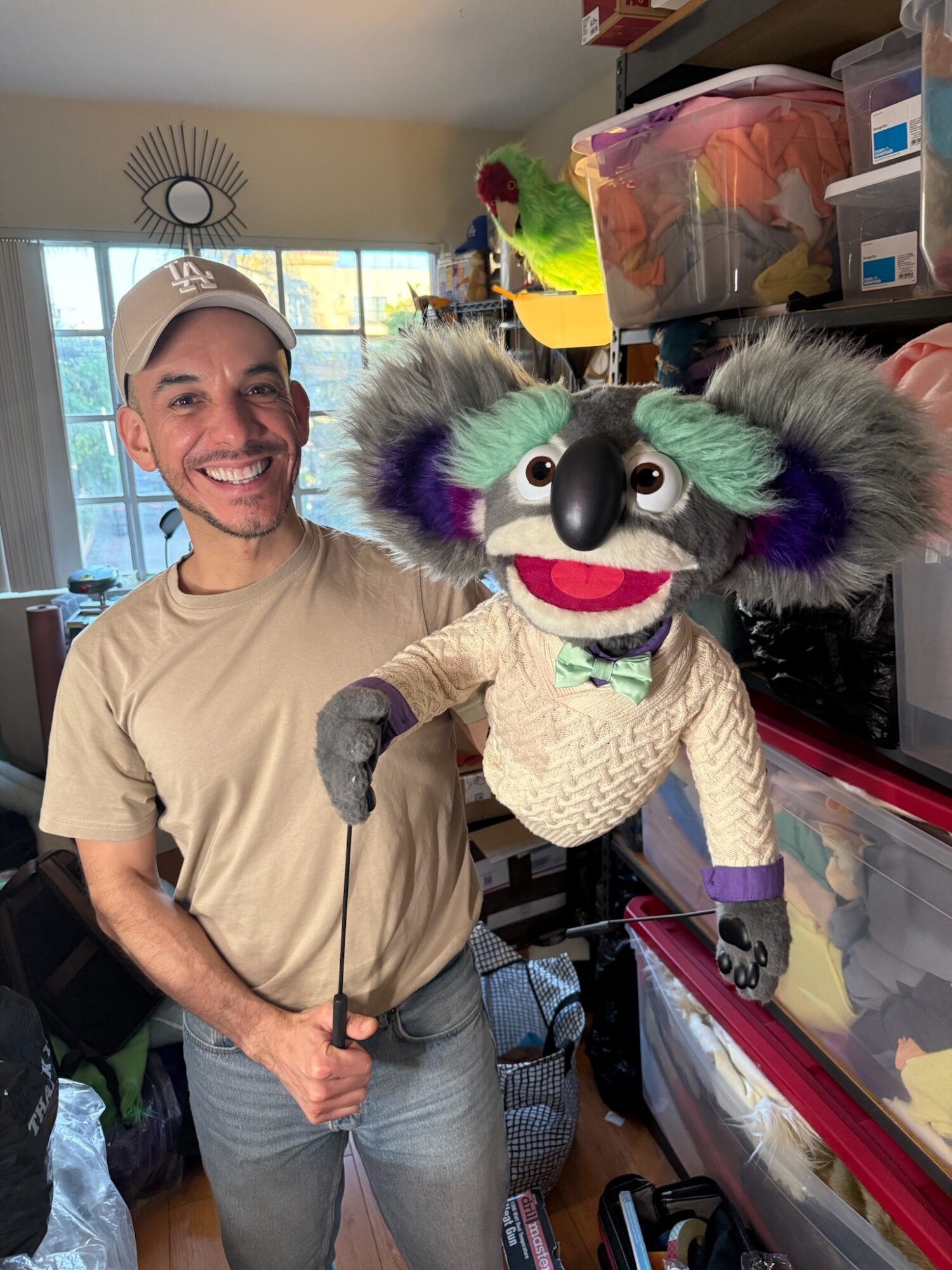 Man smiling with a puppet resembling a colorful, furry creature with big eyes and a wide mouth.