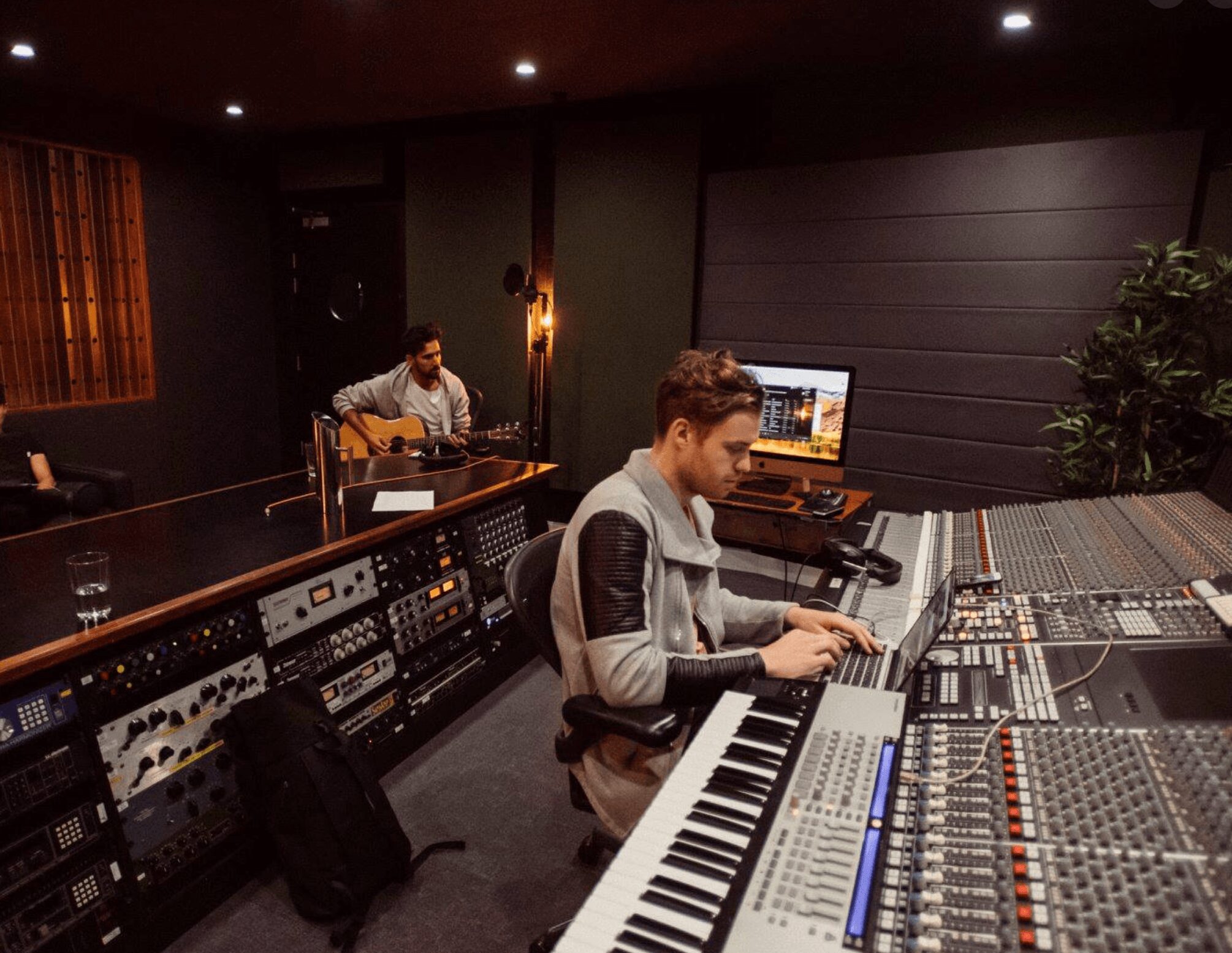 Person working at a music mixing console in a recording studio with equipment and a computer screen.