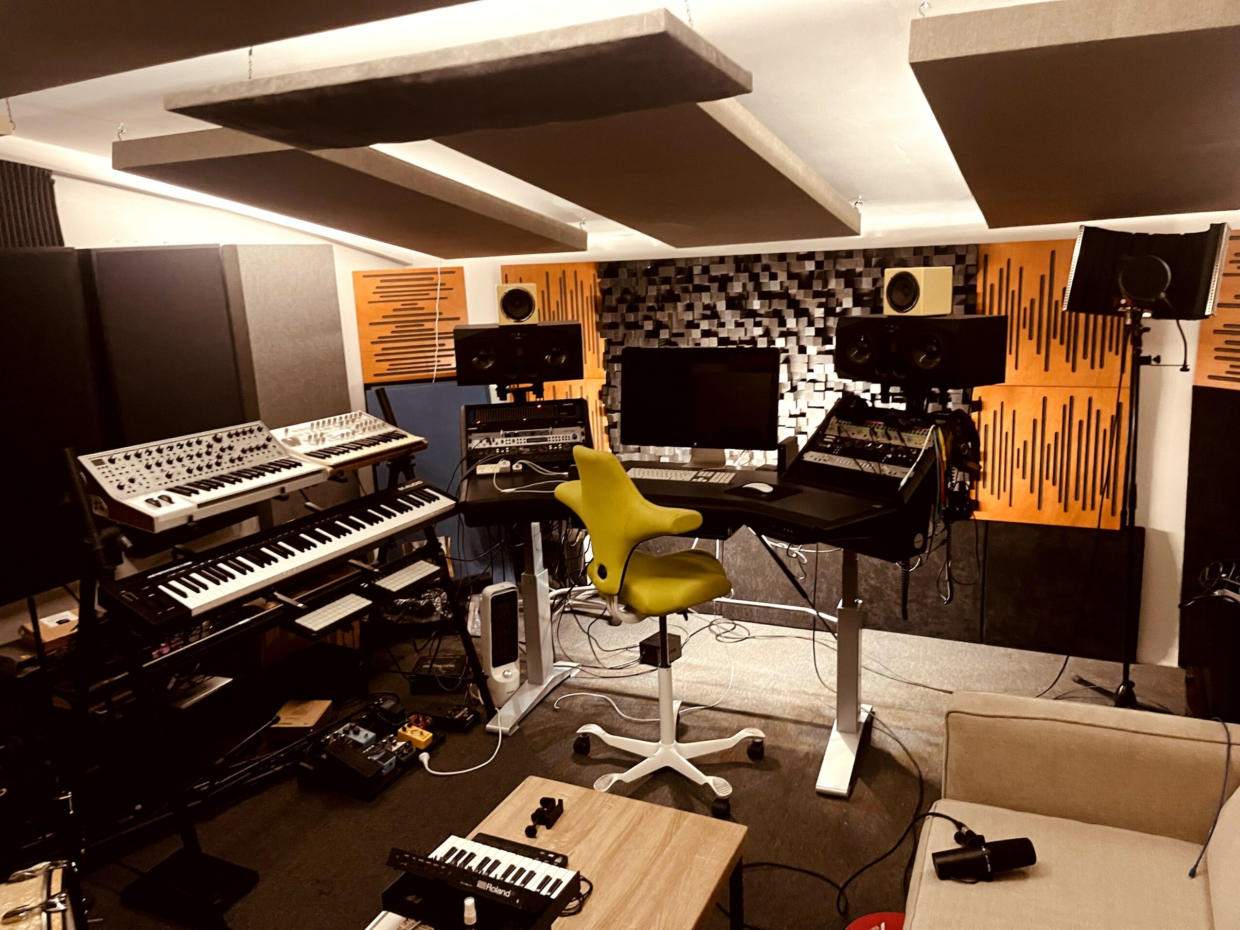 Music studio with keyboards, monitors, and a yellow chair in a room with acoustic panels.