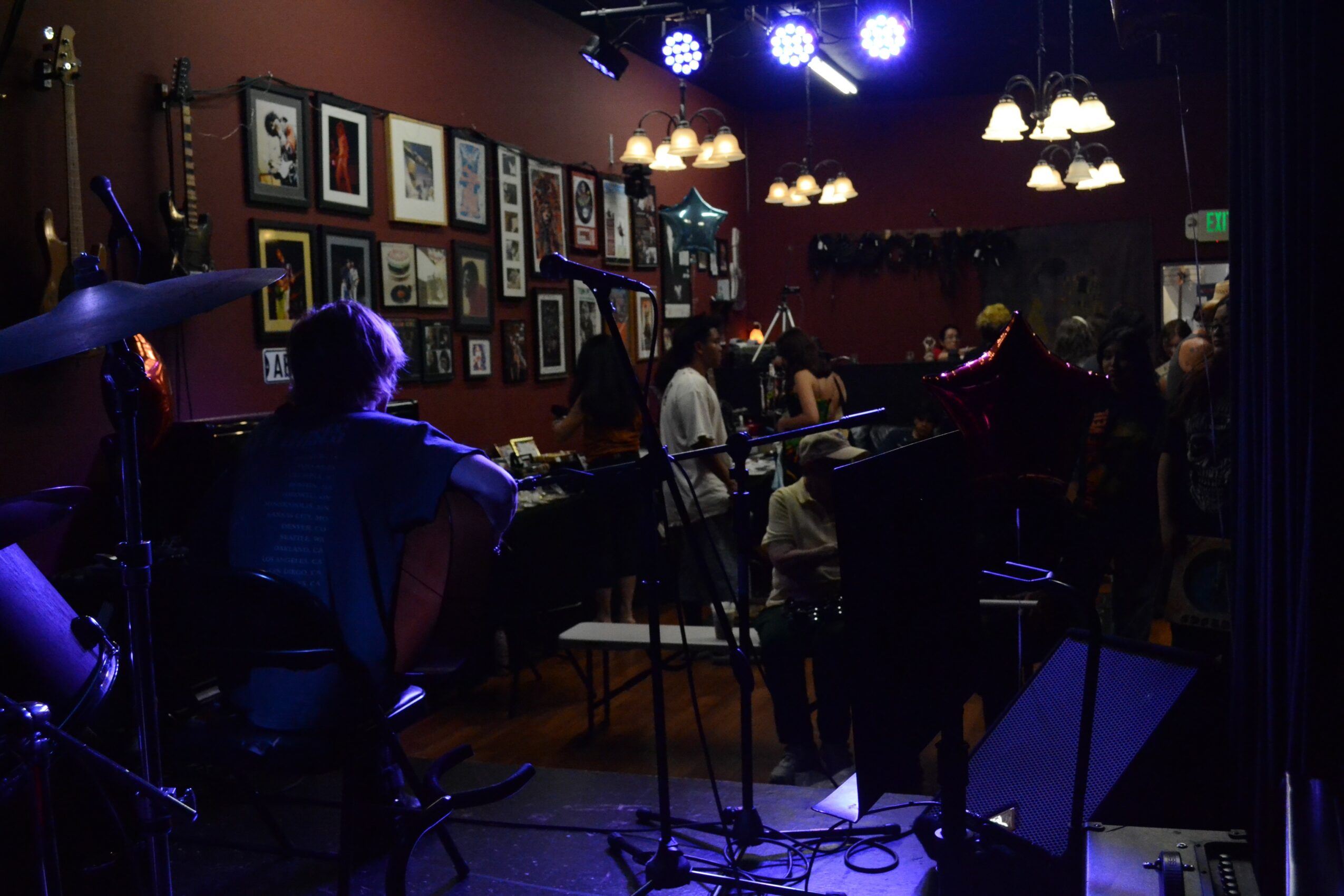 People sitting at tables in a dimly lit room with framed pictures on the wall and hanging lights.