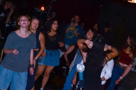 Group of people dancing and socializing in a dark indoor setting with colorful lighting.