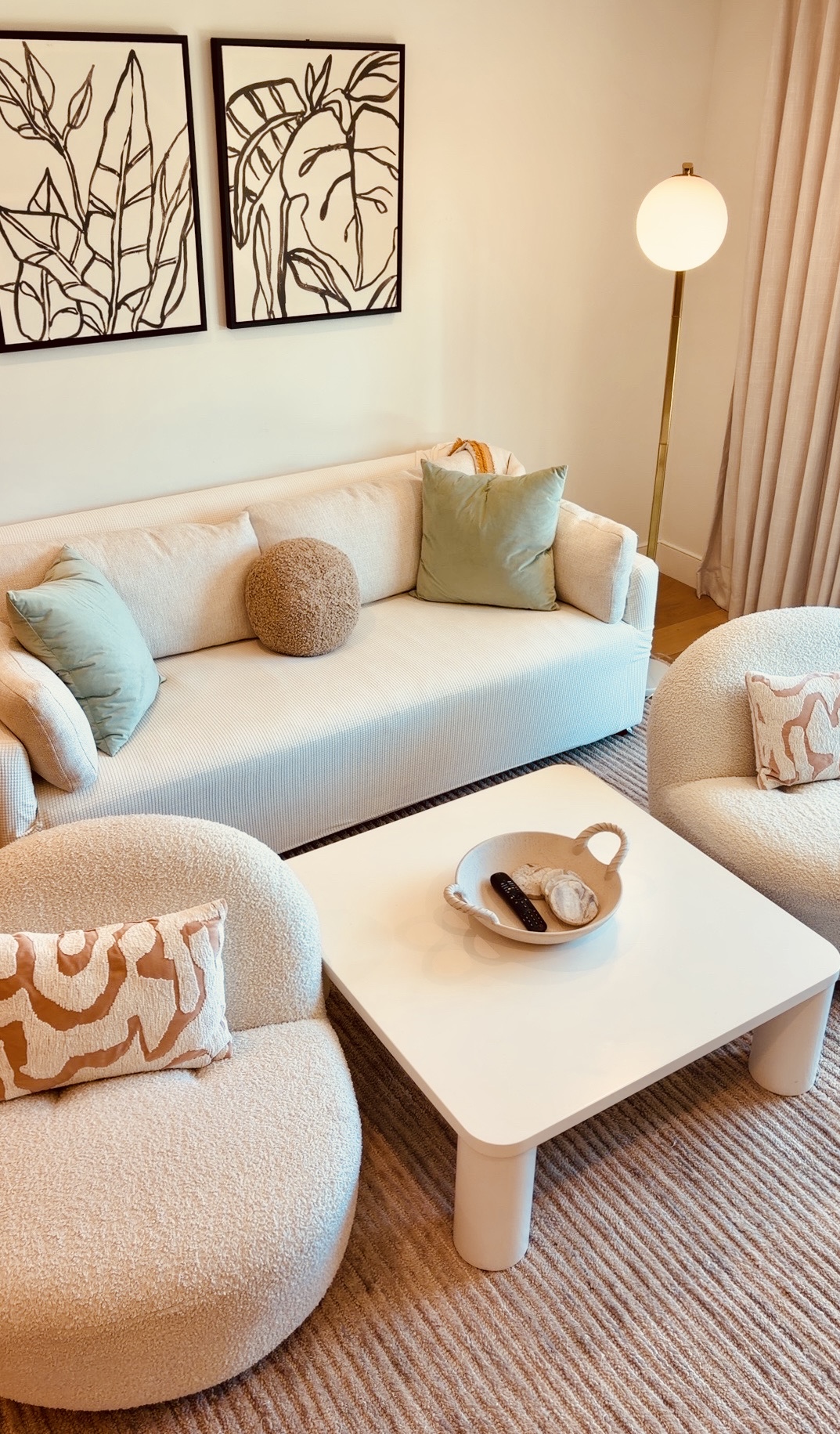 Living room with a white sofa, round armchair, coffee table, and floor lamp, decorated with framed artwork and cushions.