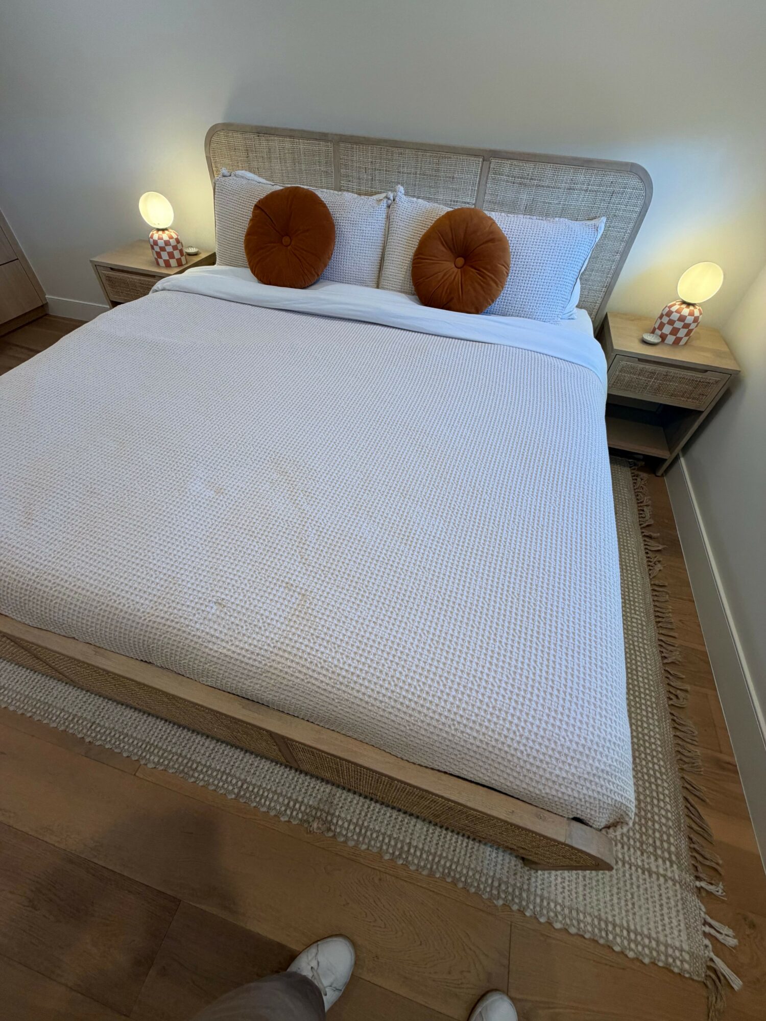 Bed with white bedding, two white pillows, two round brown cushions, and a woven headboard in a bedroom.