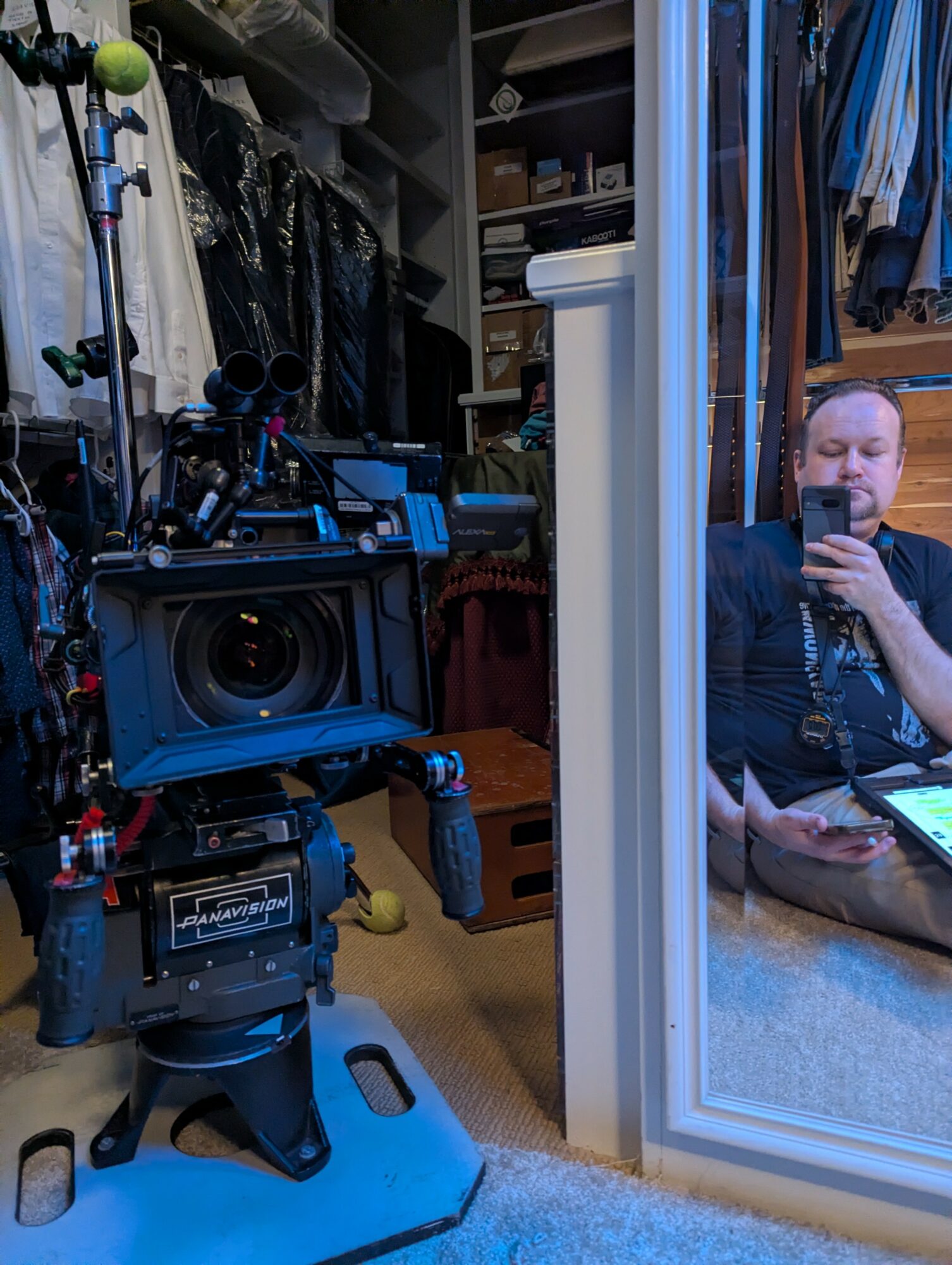 Person sitting on the floor taking a selfie in a closet with clothes and a camera setup nearby.