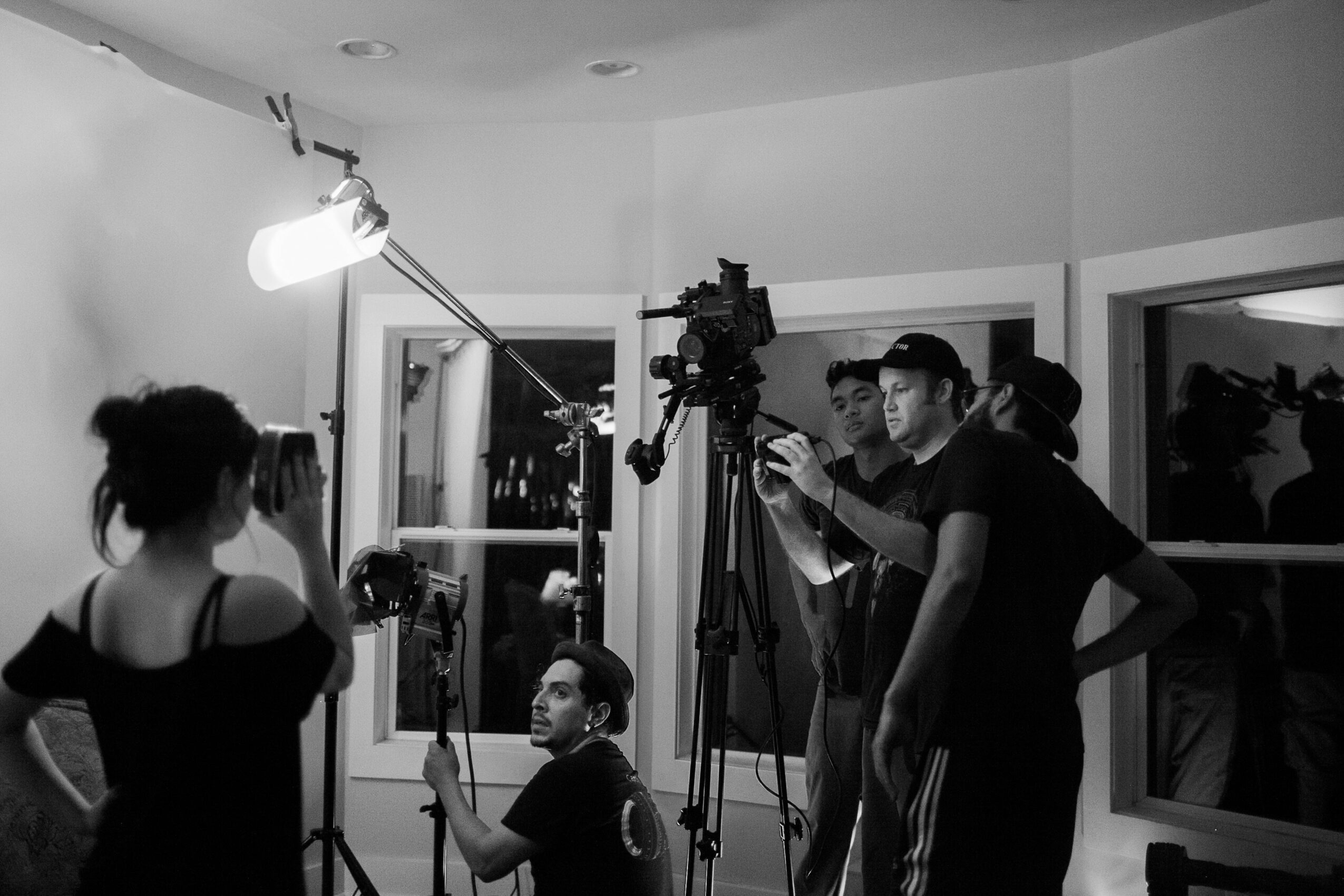 Group of people in a room with camera equipment, some looking at a woman with her back to the camera.