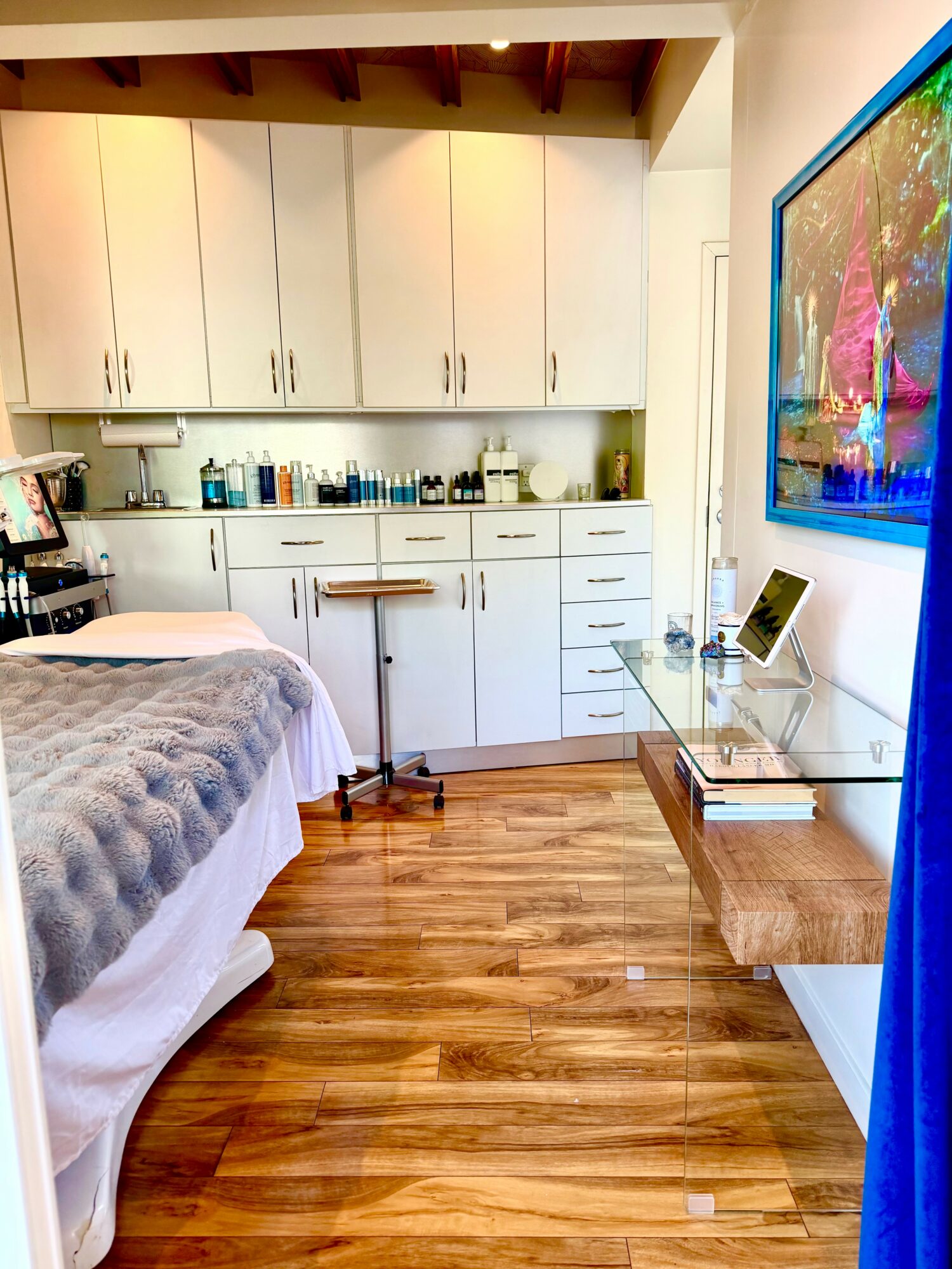 Bedroom with white cabinets, bed with gray blanket, wooden floor, glass desk, and a colorful wall art.