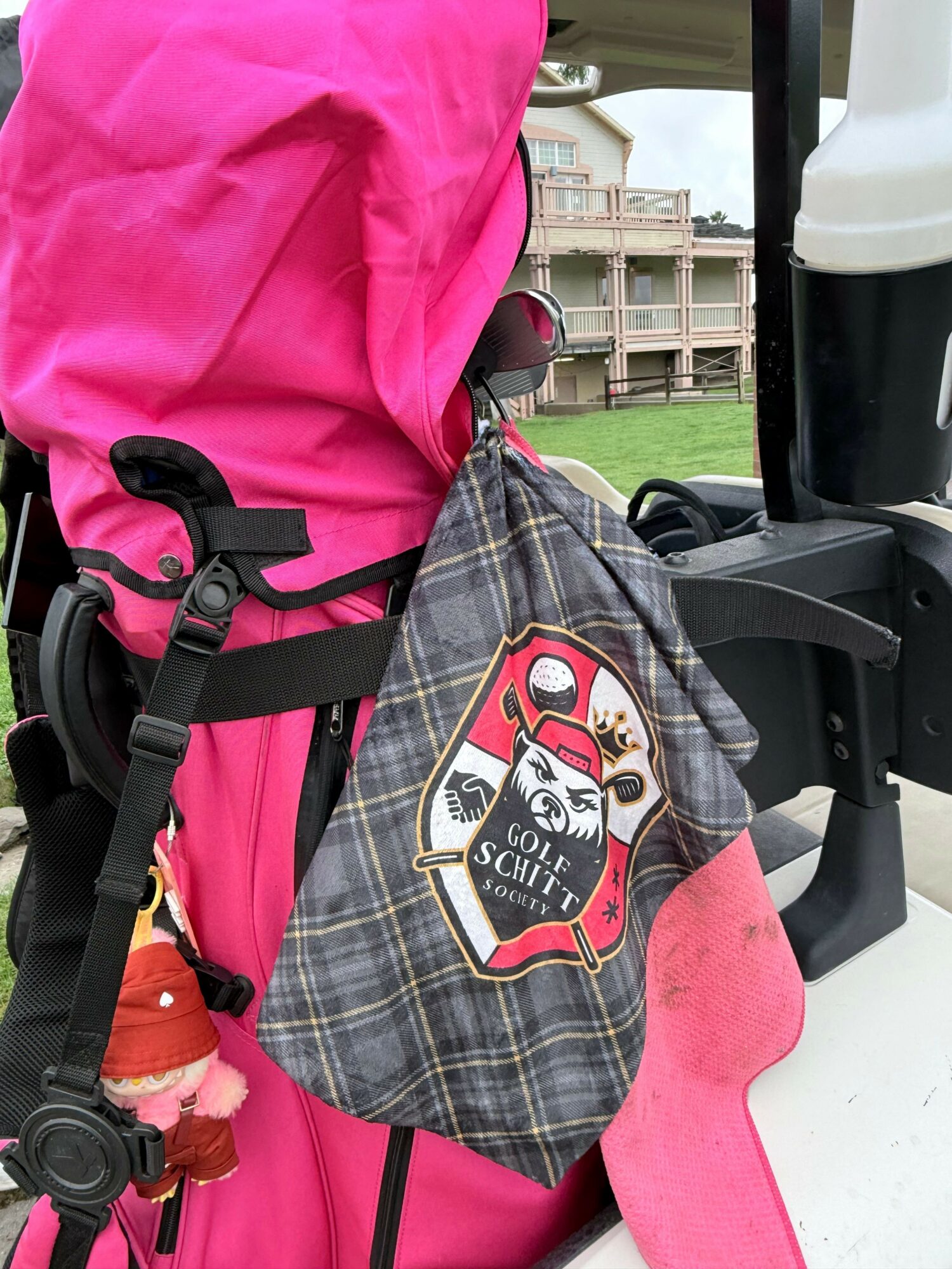 Golf cart with a pink cover and a plaid bag hanging on the side, with a patch and a small doll attached.