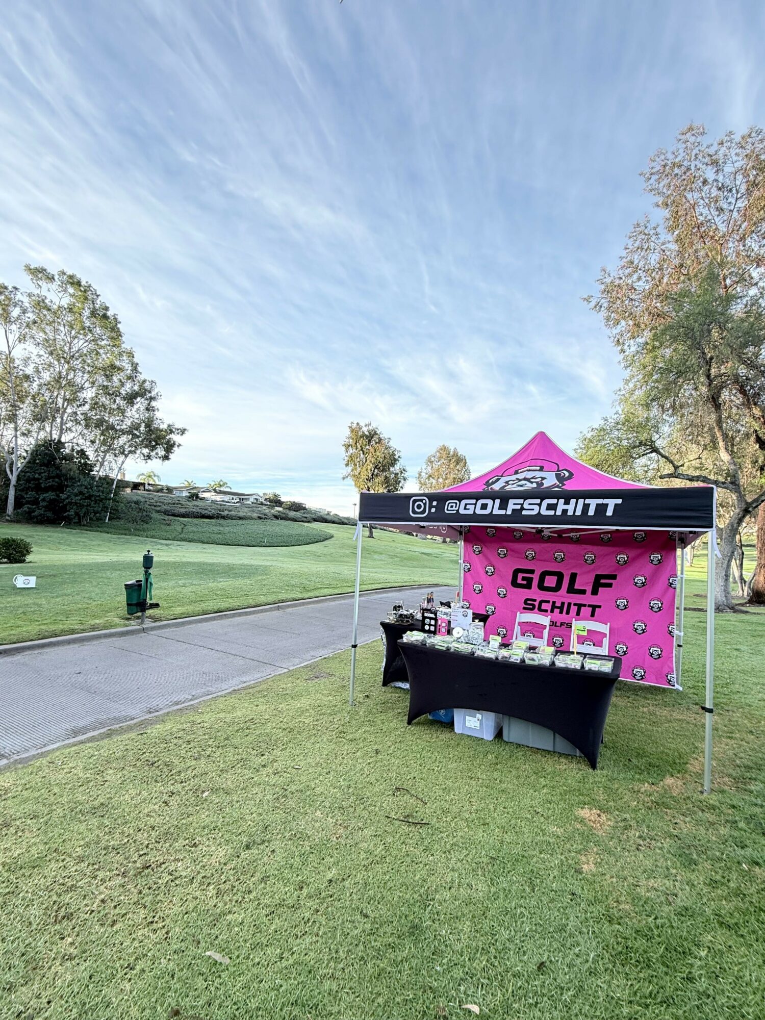 Golf course with a tent and table set up on the grass, trees, and a partly cloudy sky.