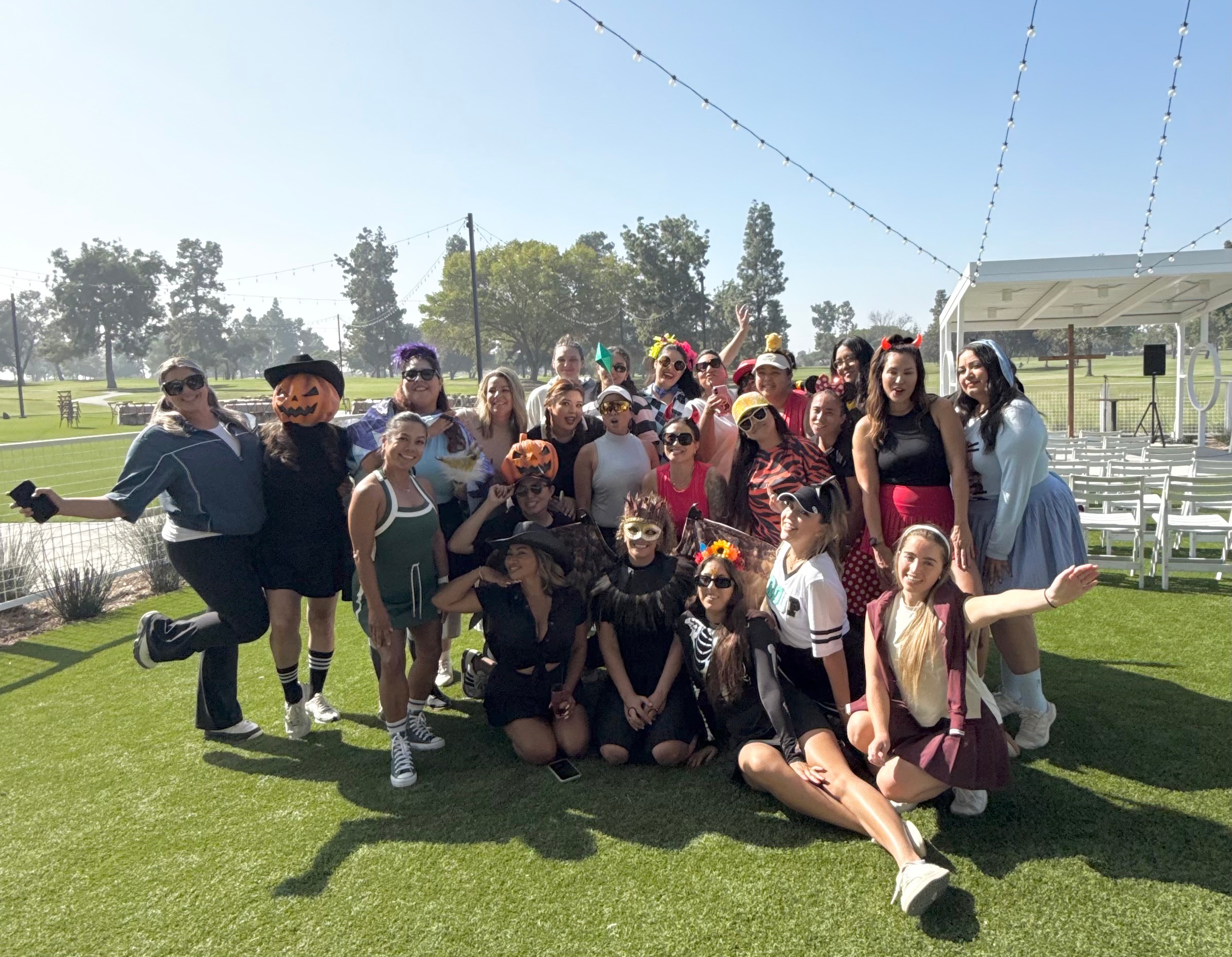 Group of children and adults outdoors on grass, some wearing costumes, posing for a photo.