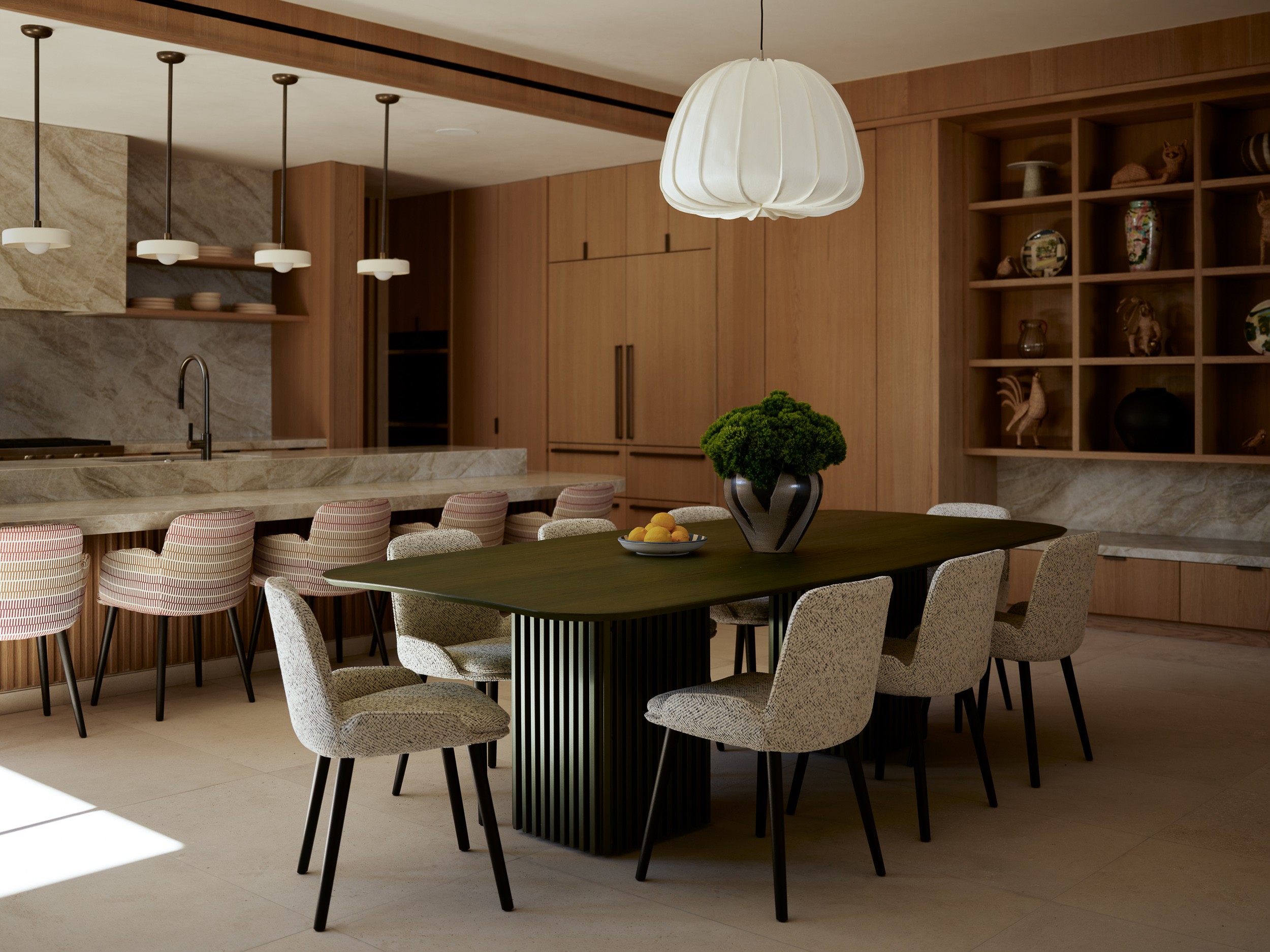 Dining room with a dark table, six light-colored chairs, a hanging lamp, and wooden shelves on the wall.