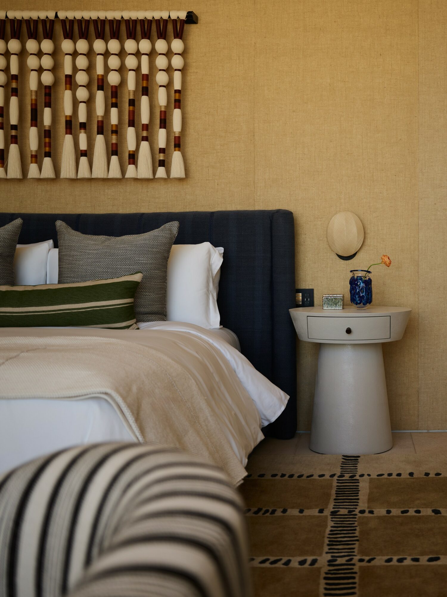 Bedroom with bed, pillows, nightstand, and wall decor, beige wall background, striped blanket in foreground.