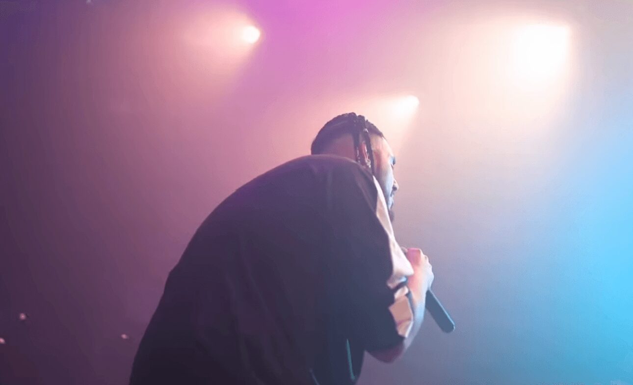 Person holding a microphone on stage with colorful lighting and fog effects.
