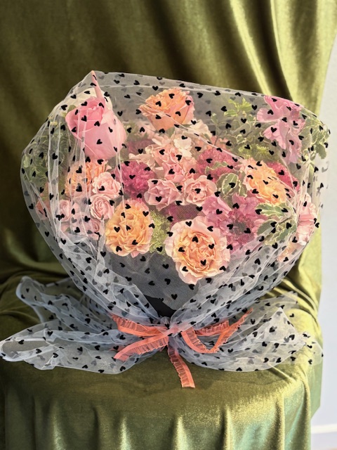 Bouquet of pink, peach, and yellow flowers wrapped in polka dot paper with a pink ribbon bow.