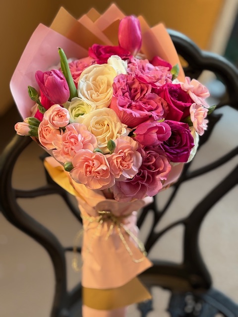 Colorful bouquet of pink, white, and purple flowers wrapped in pink paper, placed on a black metal surface.