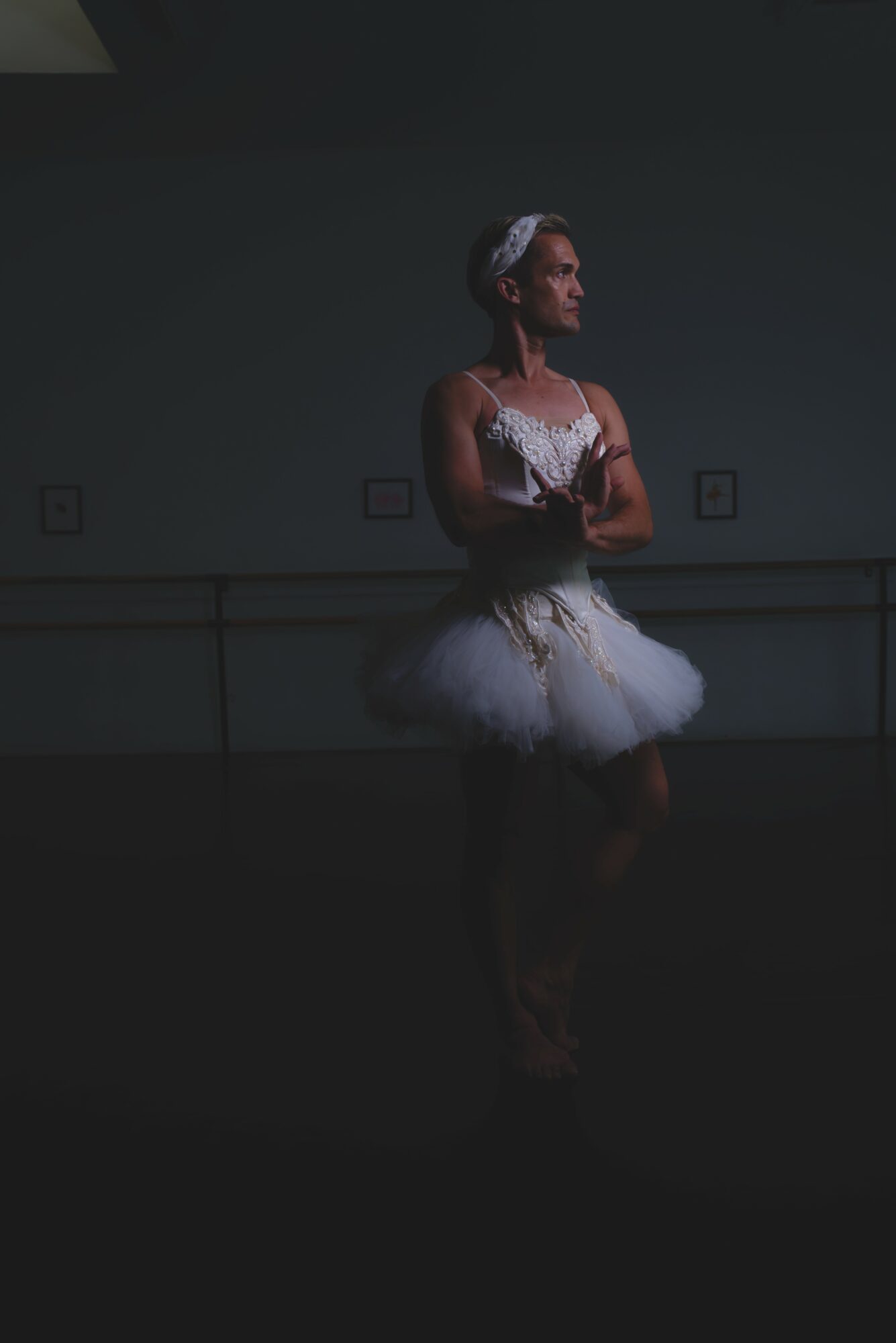 Ballet dancer in costume standing in a dark room, arms crossed, looking to the side.
