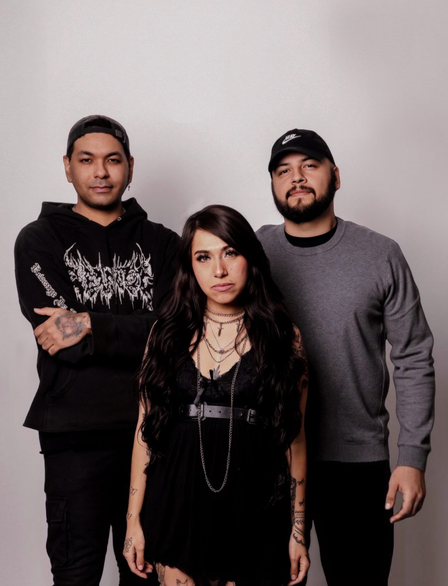 Three people standing against a plain background, two men and one woman, all facing forward.