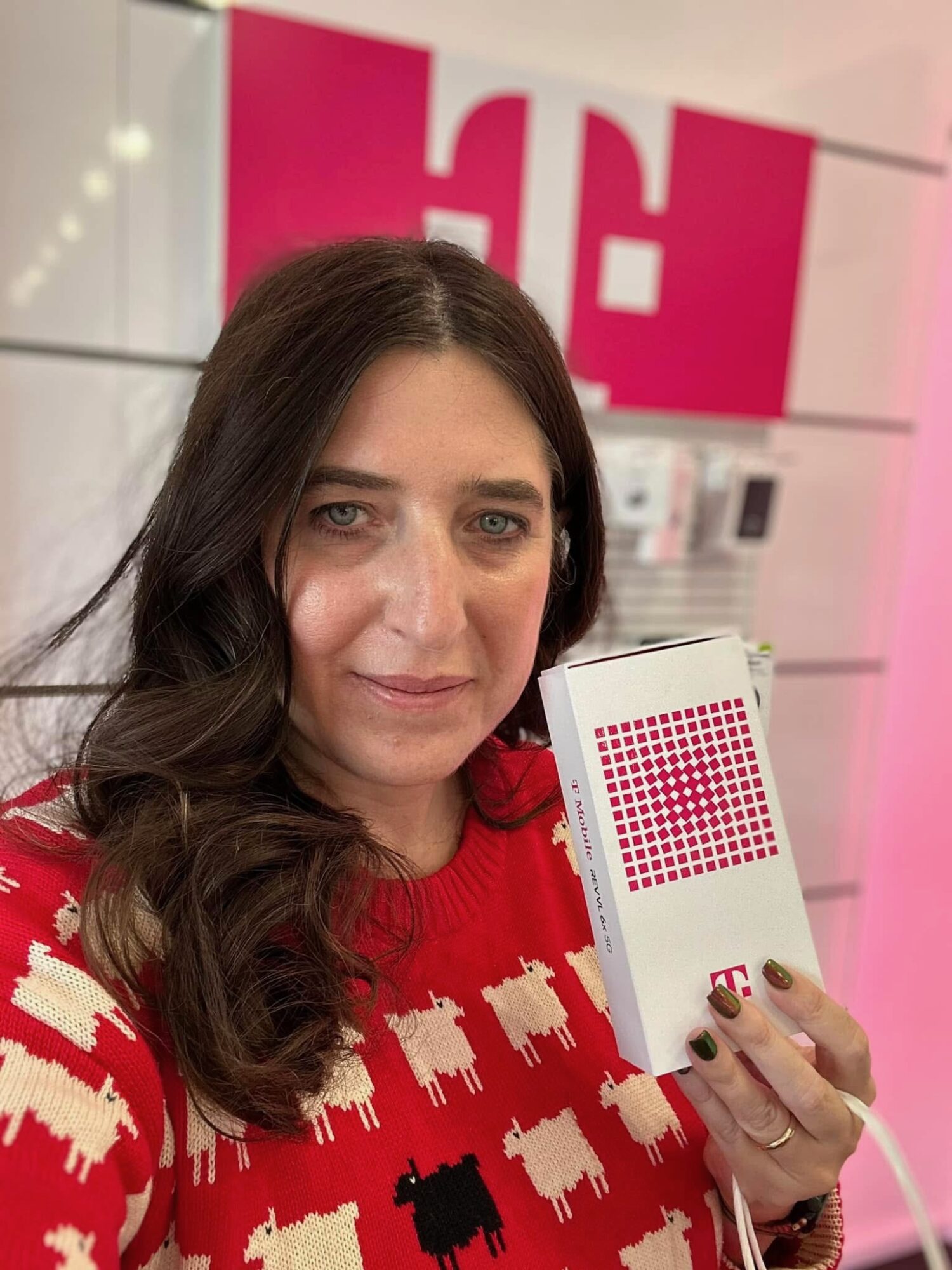 Woman with long dark hair holding a color palette, wearing a red sweater with white sheep pattern, in a store.
