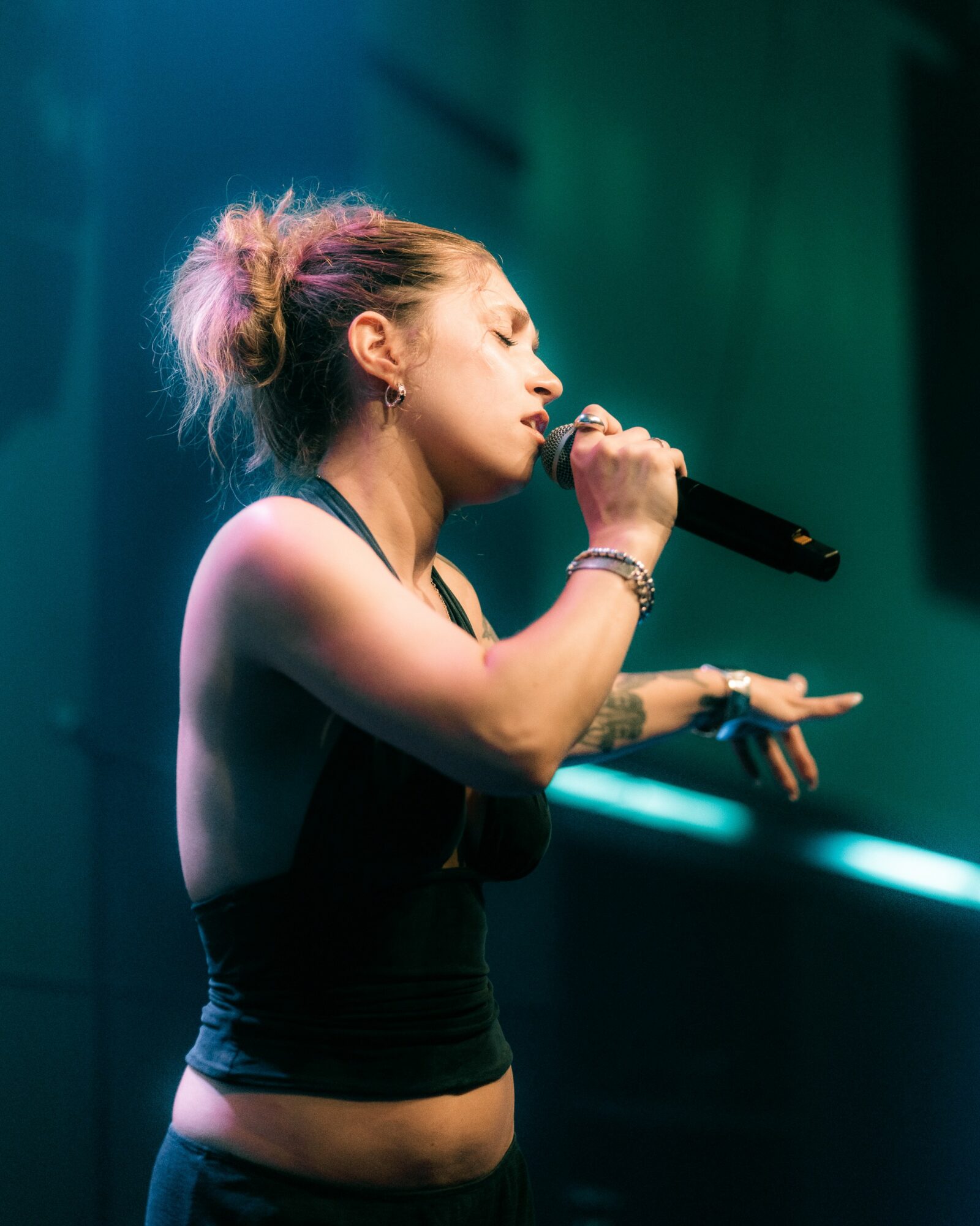 Woman singing into microphone with eyes closed, stage lighting in background.