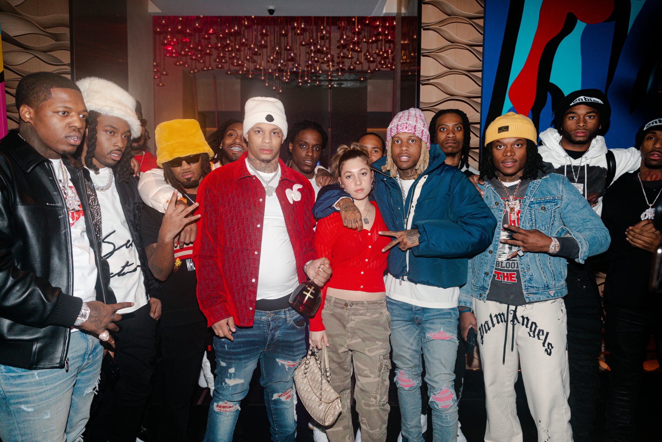 Group of people posing indoors, some wearing hats and casual clothing, with colorful background art.