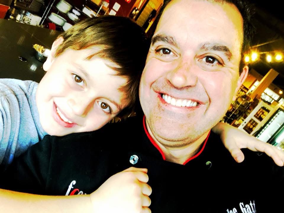 Two people smiling, one with arm around the other, in a bar or restaurant setting.
