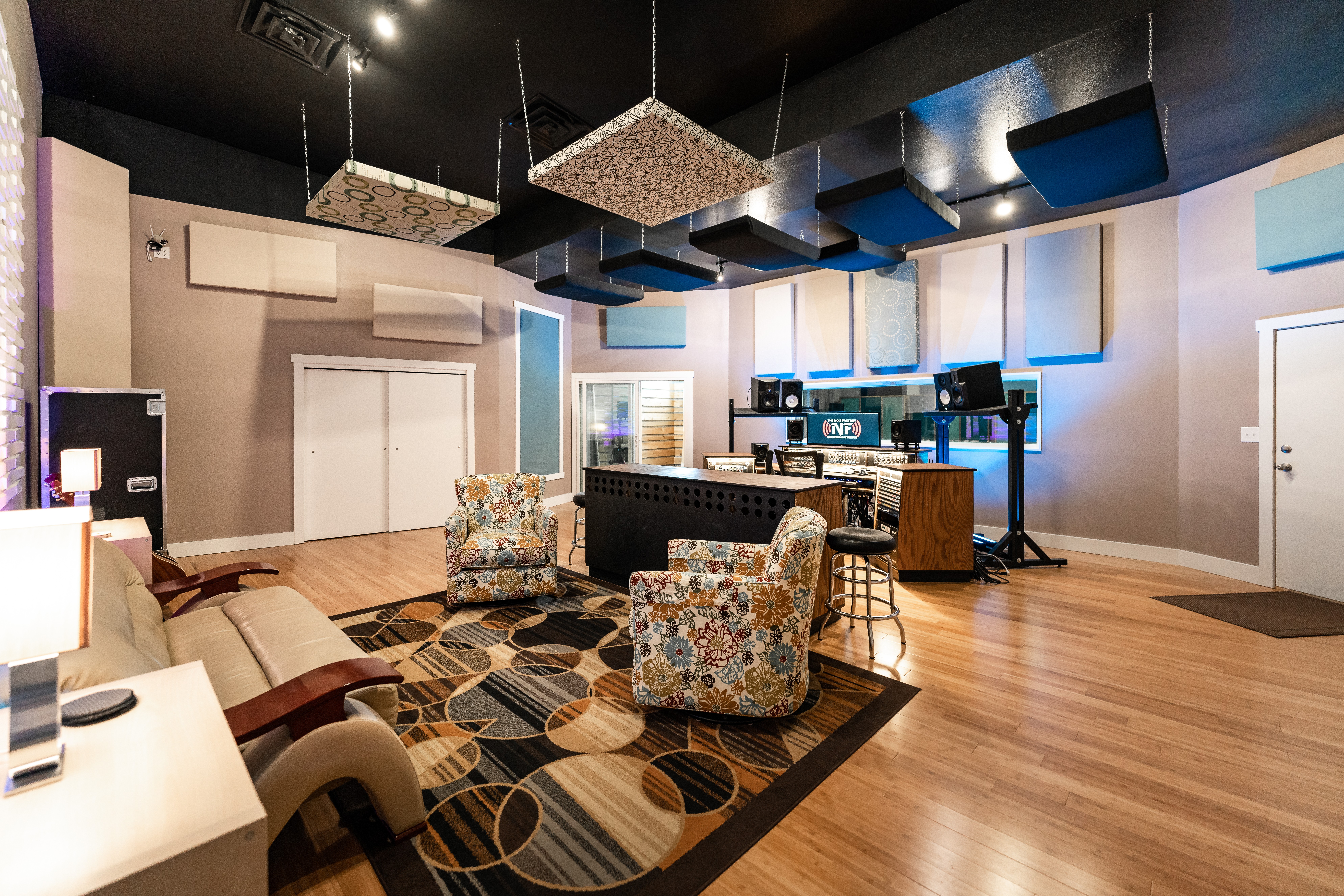 Modern music studio with chairs, a rug, and audio equipment in a spacious room with wooden floors.