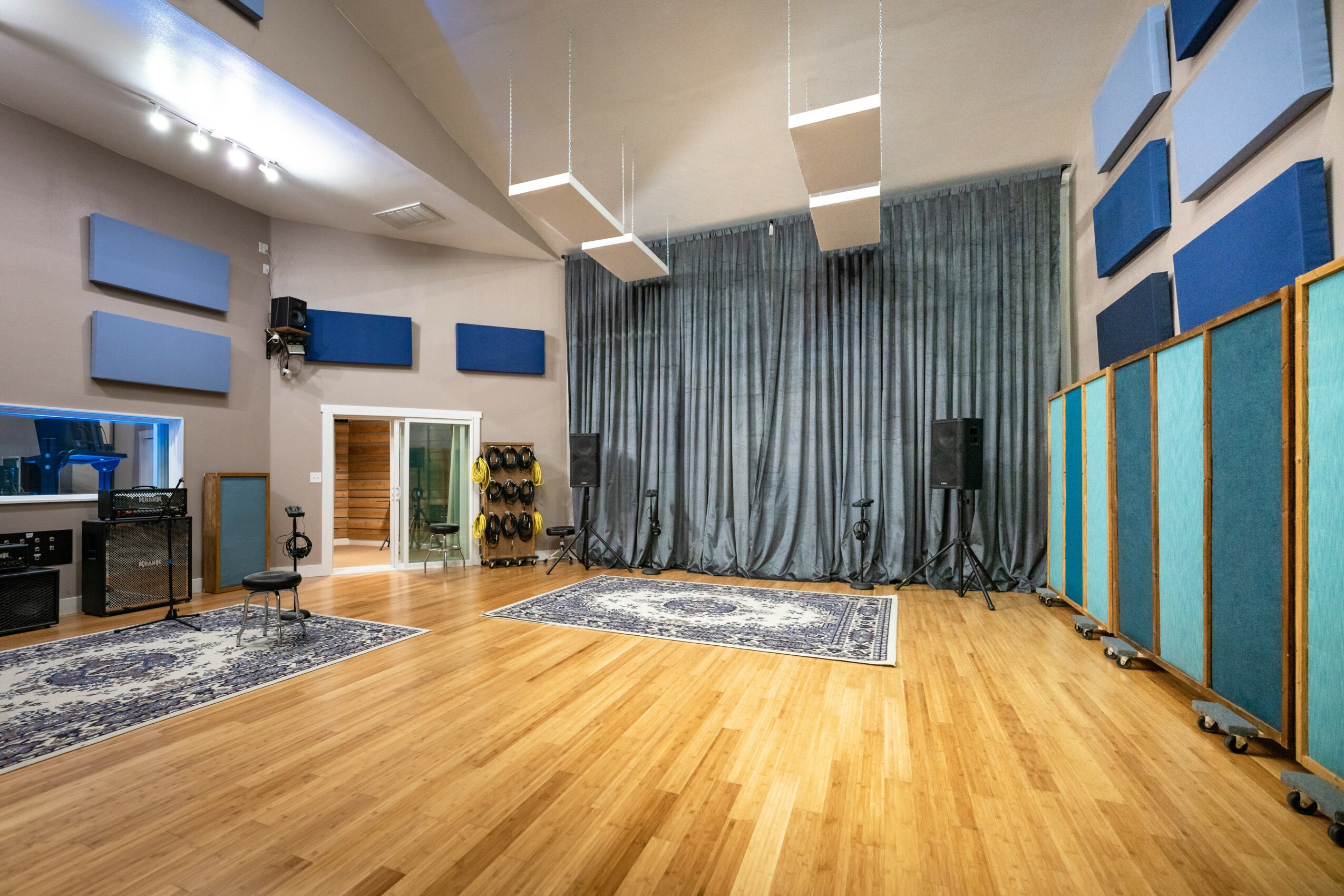 Large room with wooden floor, blue curtains, soundproof panels, and audio equipment, possibly a recording or rehearsal space.