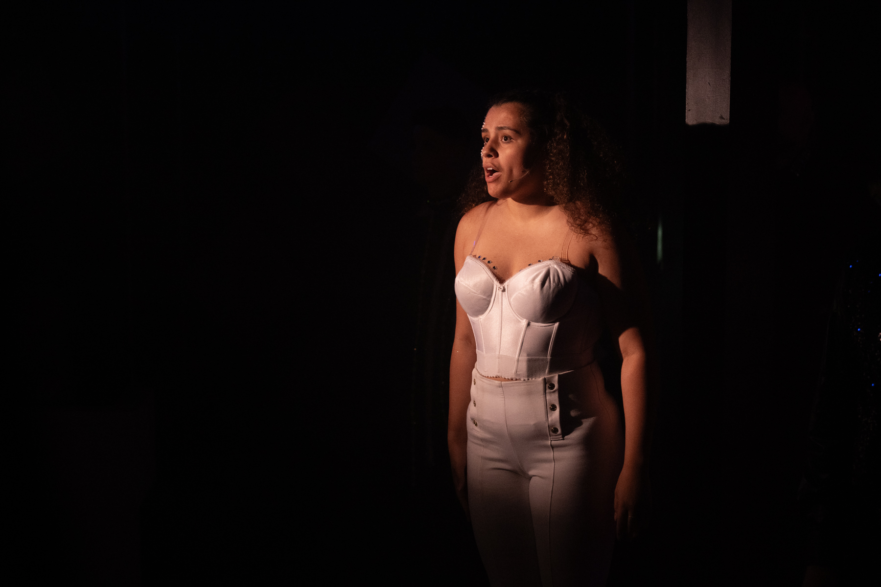 Woman in a strapless white dress standing on stage with dark background.