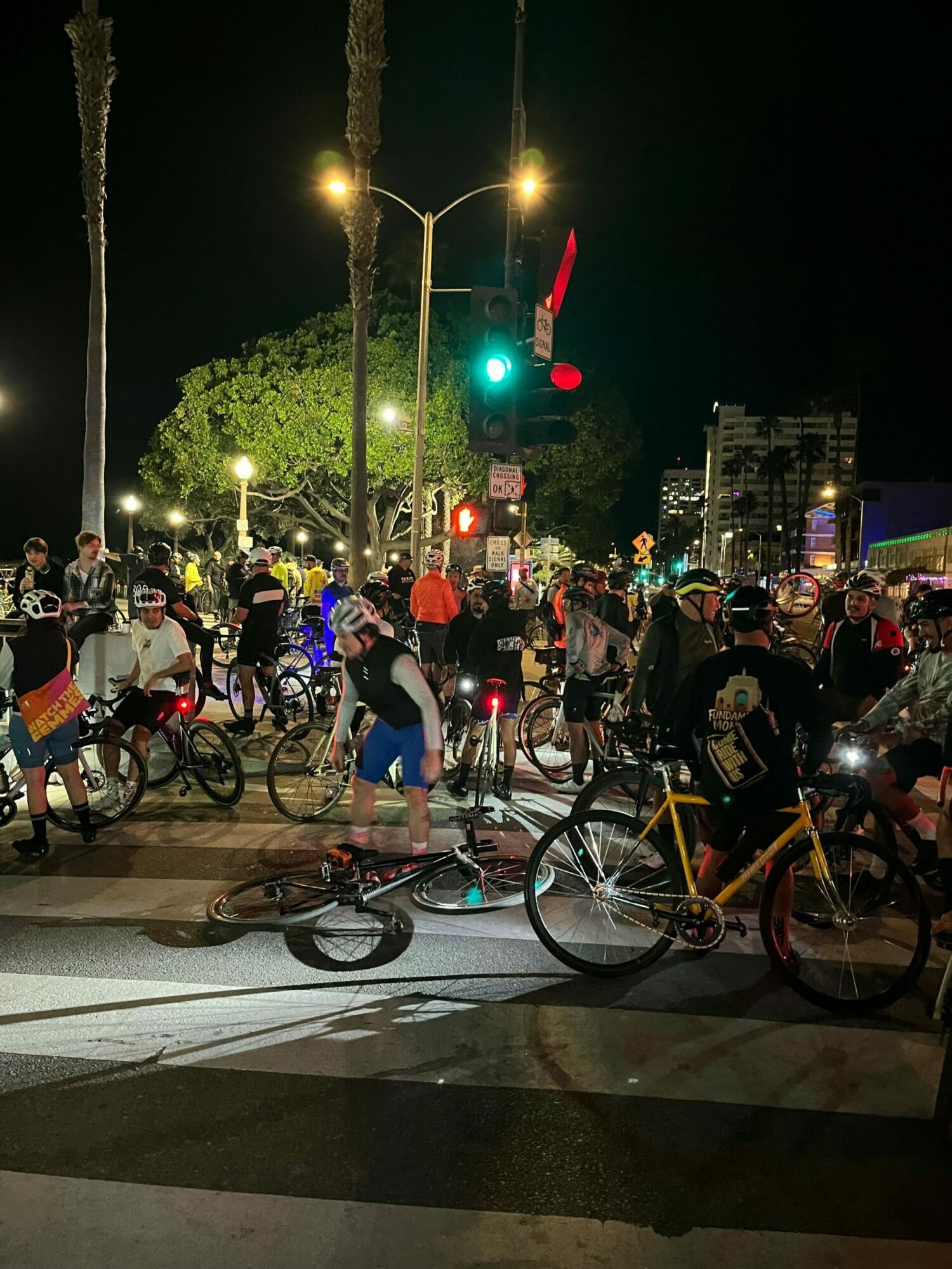 Night scene with a group of people and bicycles gathered on a city street illuminated by streetlights.