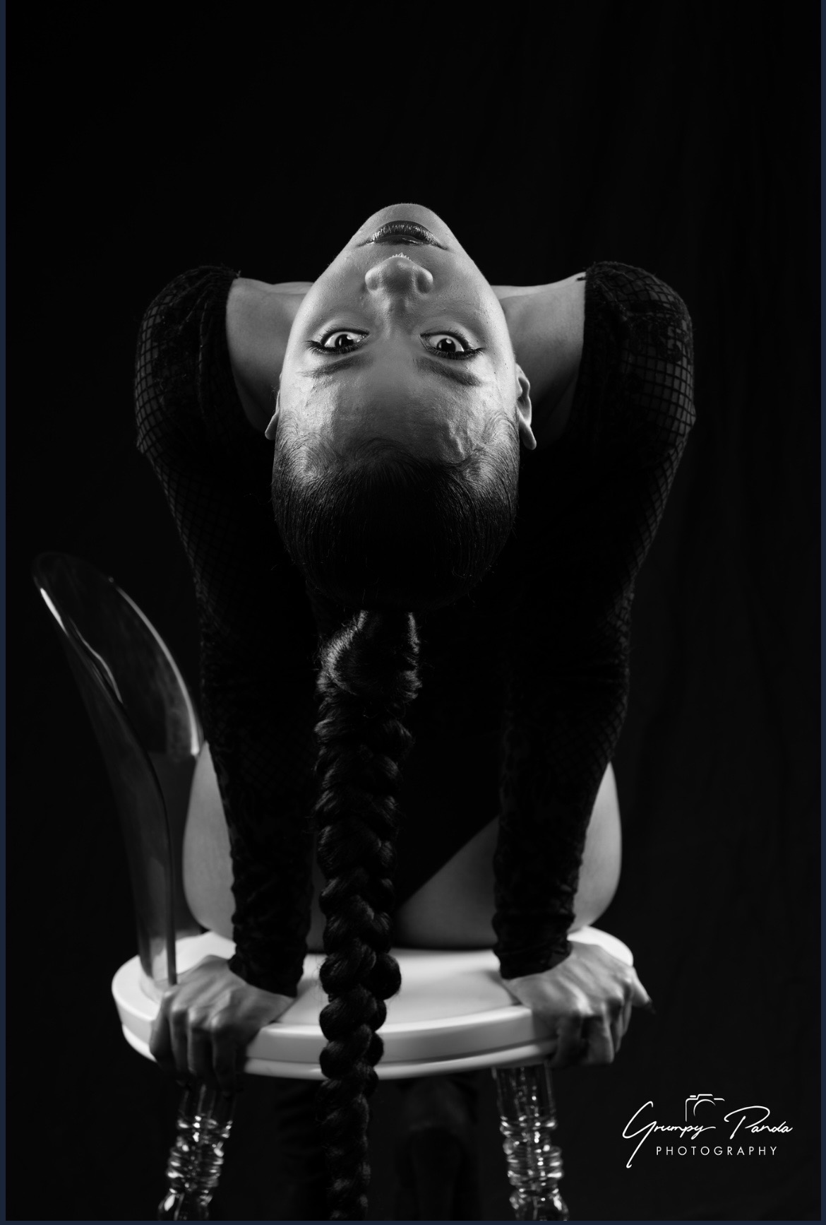 Child with braided hair leaning forward on a chair, upside down, in black and white.