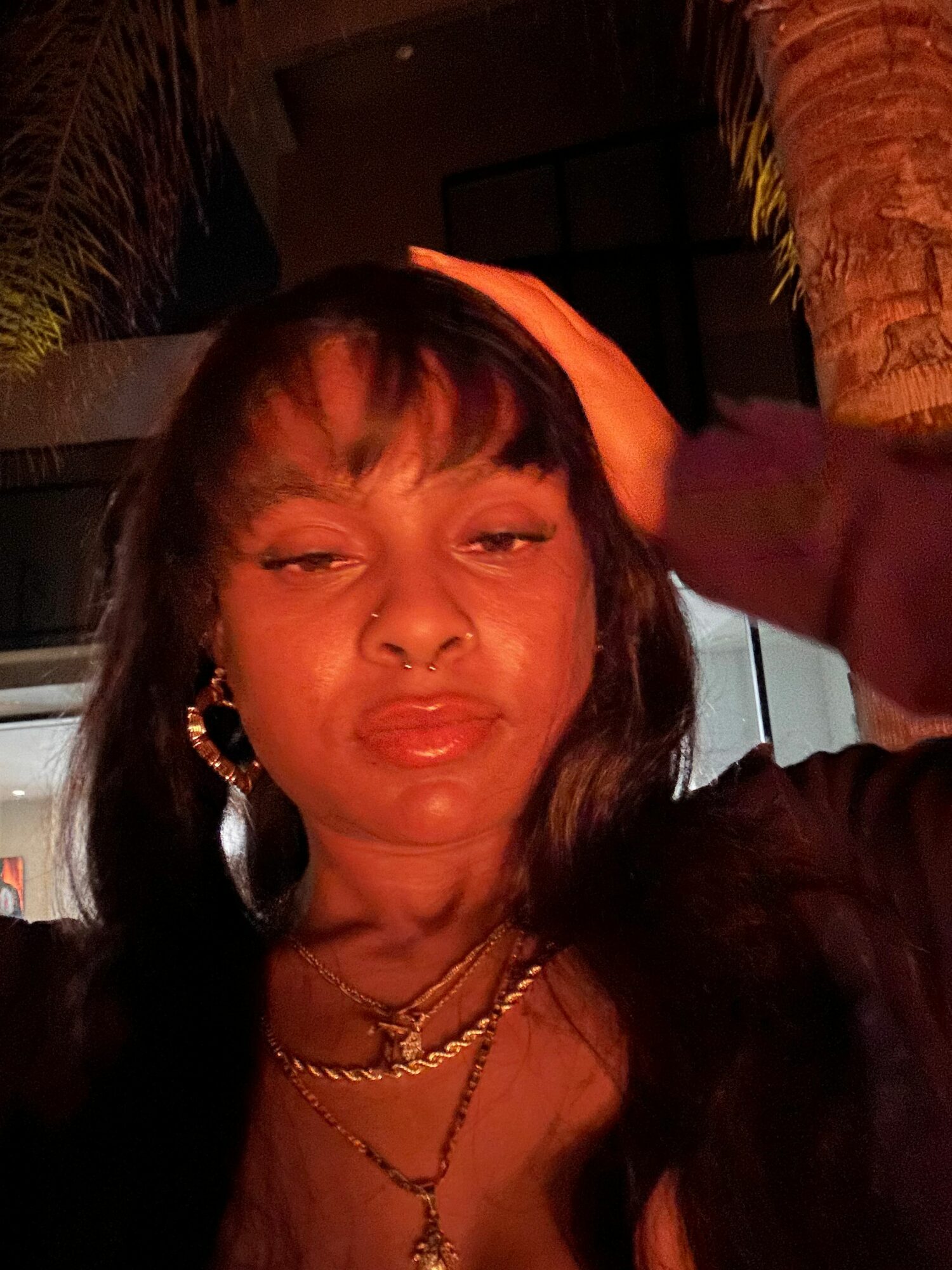 Woman with dark hair, wearing earrings and layered necklaces, posing outdoors at night.