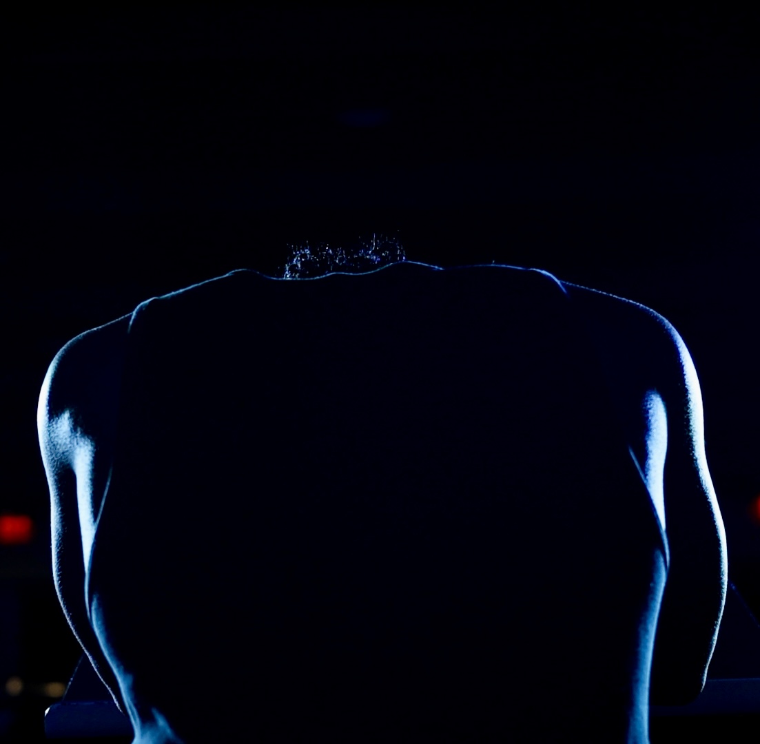 Back view of a person with illuminated shoulders and head against a dark background.