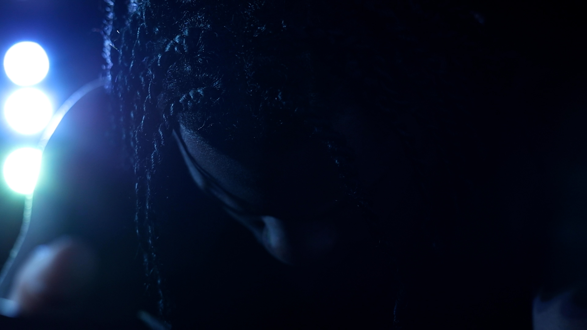 Dark image with bright light source on the left and a person's face partially visible in shadows.
