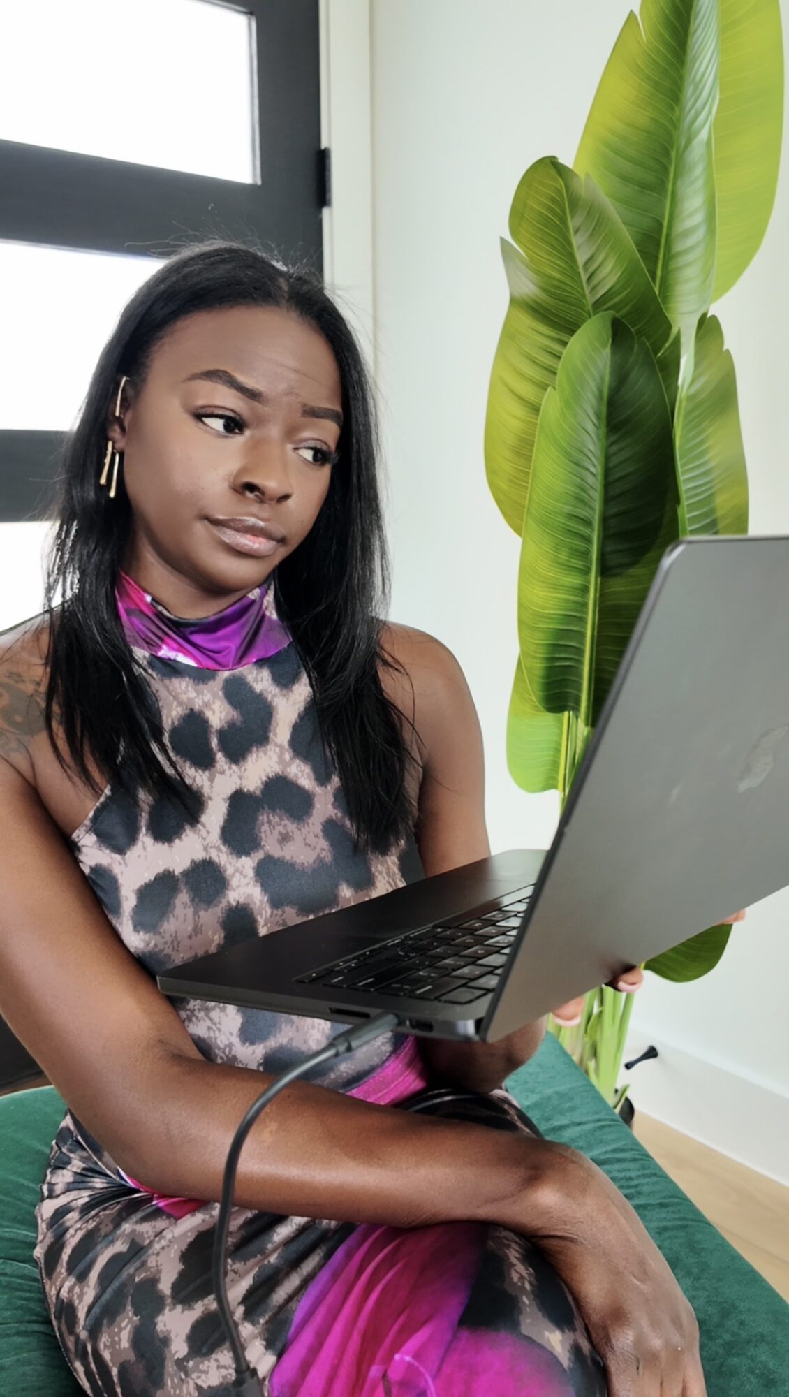 Young woman with long black hair, wearing a leopard print top and pink scarf, looking at a laptop.