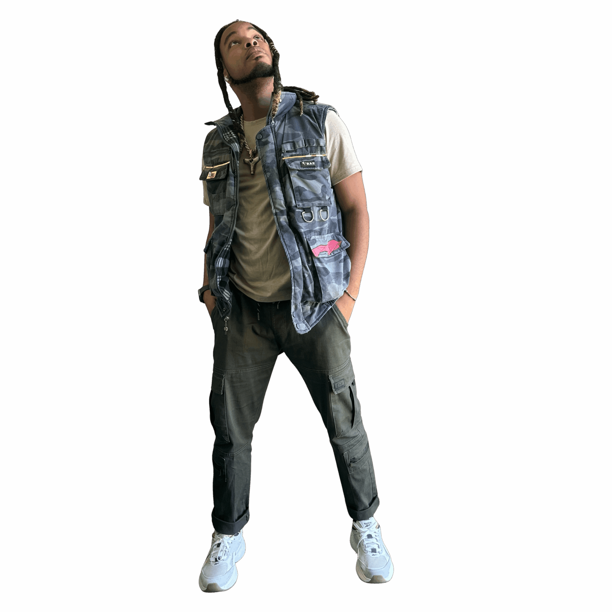 Person standing with hands in pockets, looking upward, wearing a vest, t-shirt, pants, and sneakers against a black background.