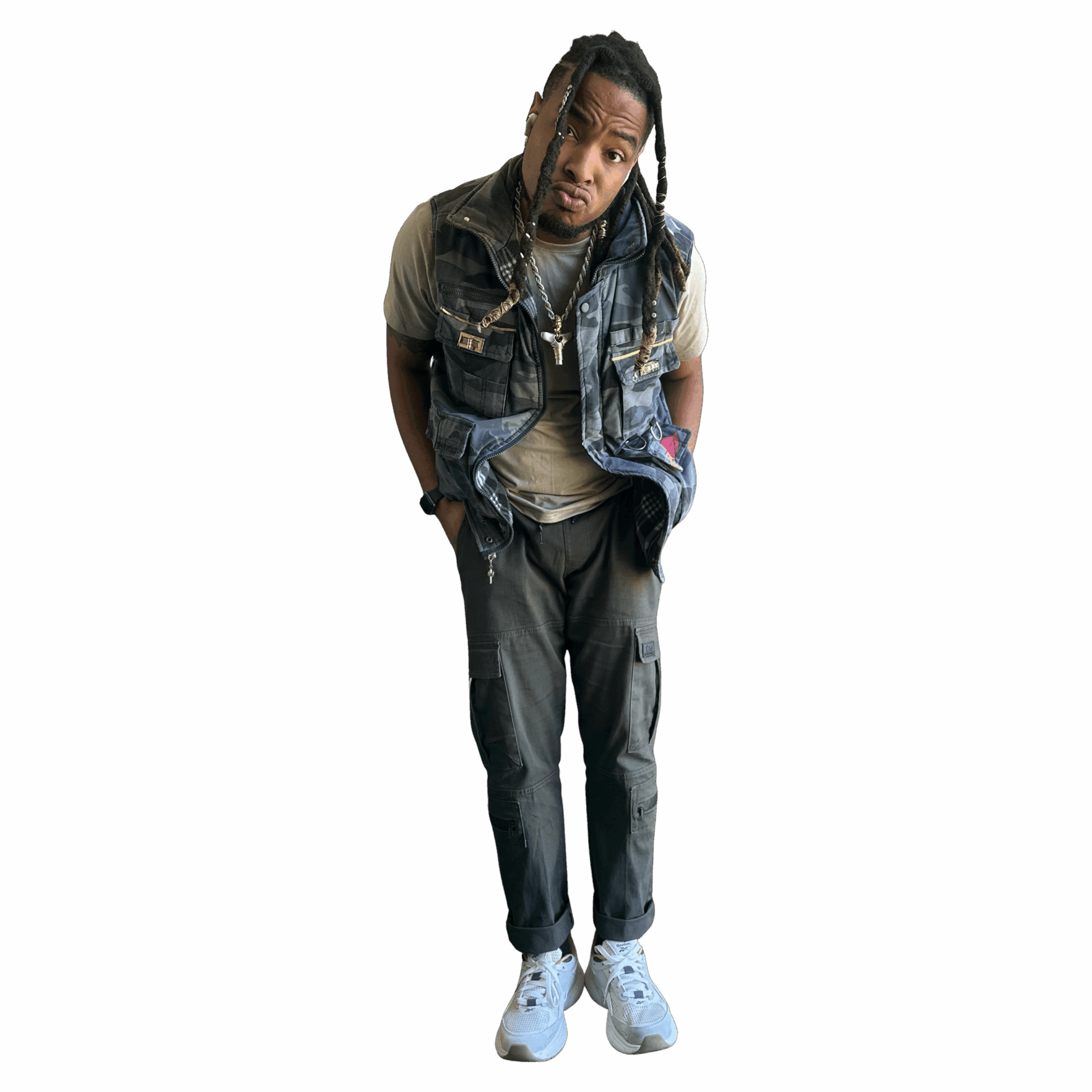 Young man with dreadlocks wearing a vest, t-shirt, cargo pants, and sneakers, standing against a black background.