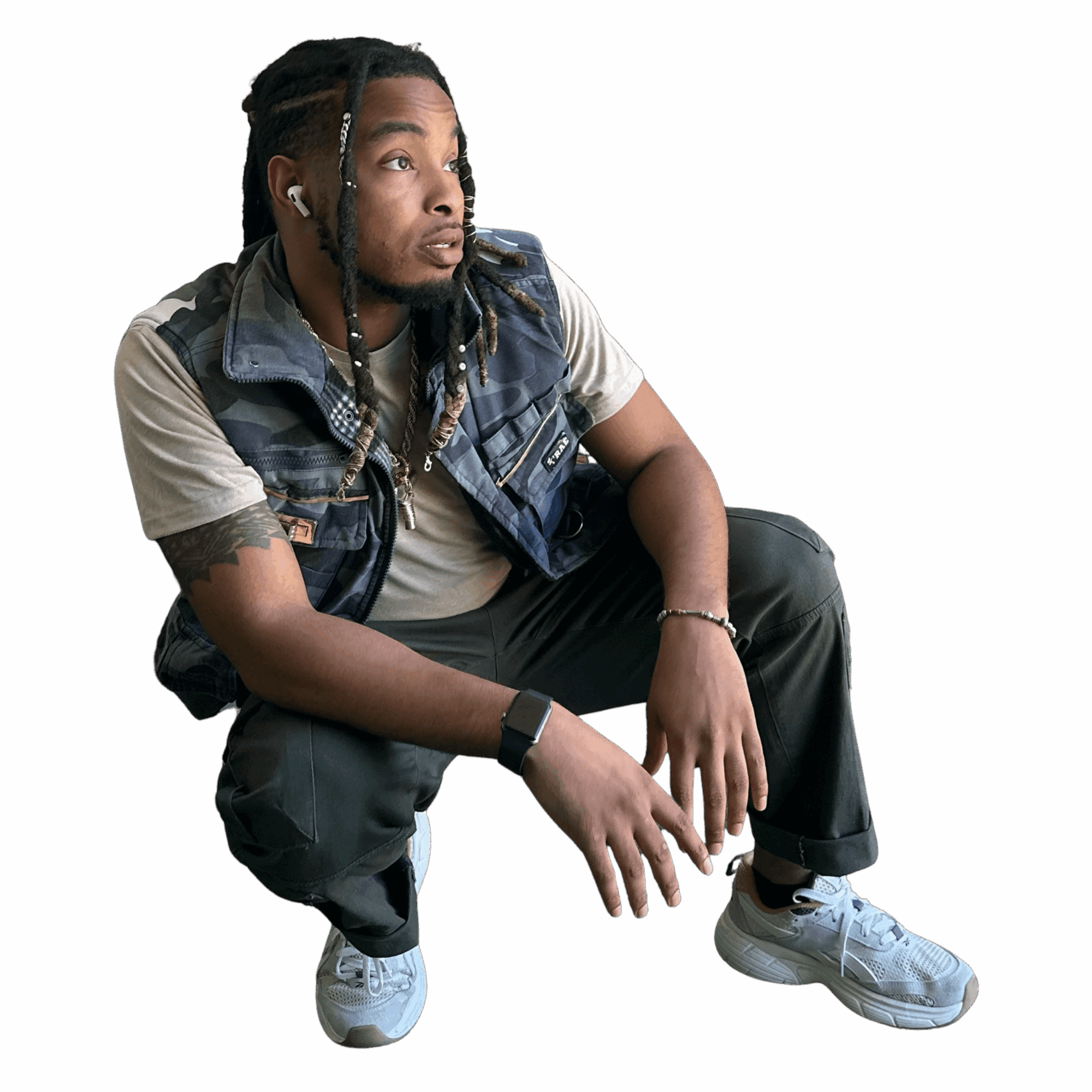 Young man with braided hair crouching, wearing a denim vest, beige t-shirt, dark pants, and white sneakers, against black background.