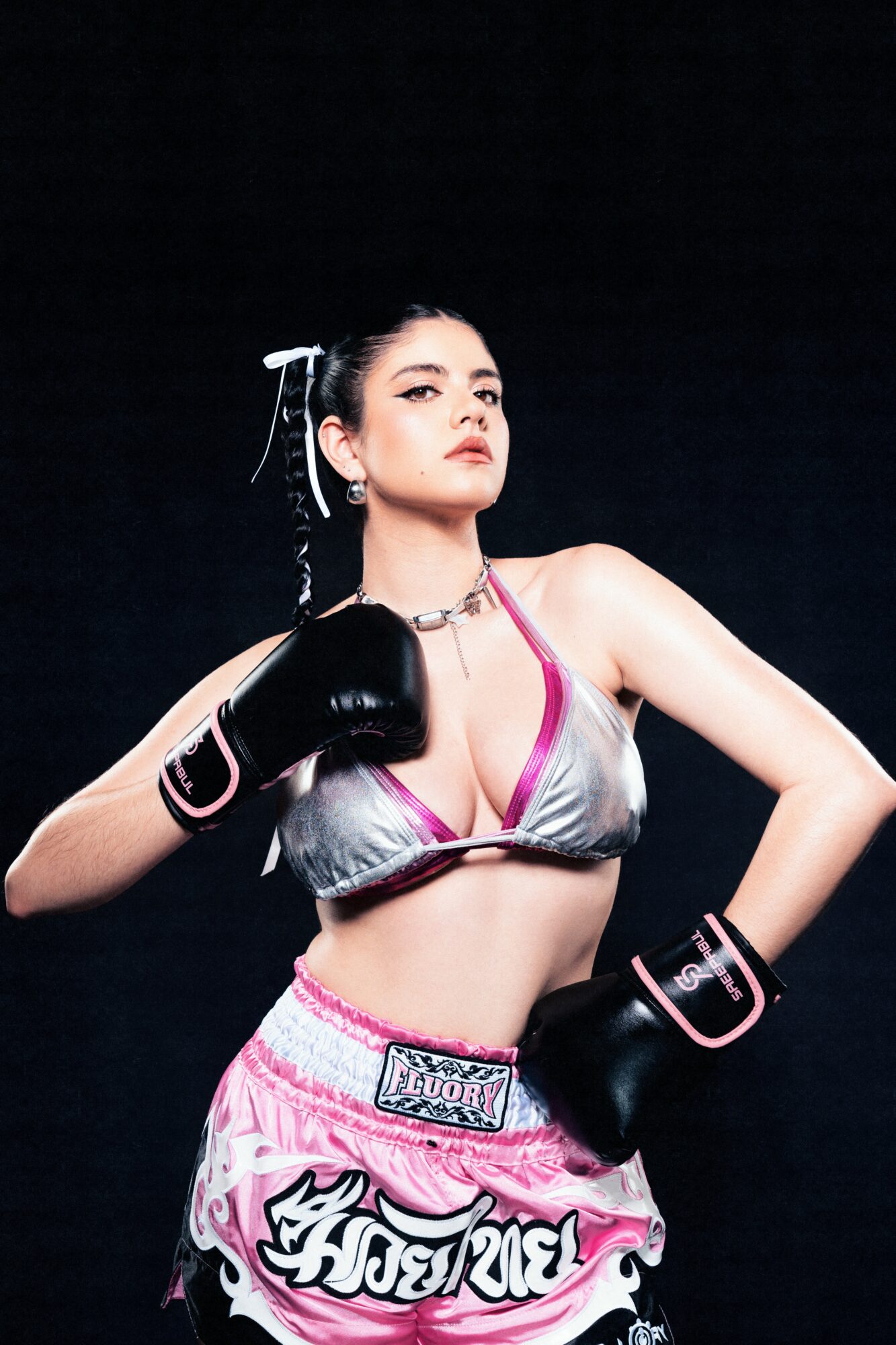 Female boxer in boxing gloves and sportswear poses confidently against a dark background.