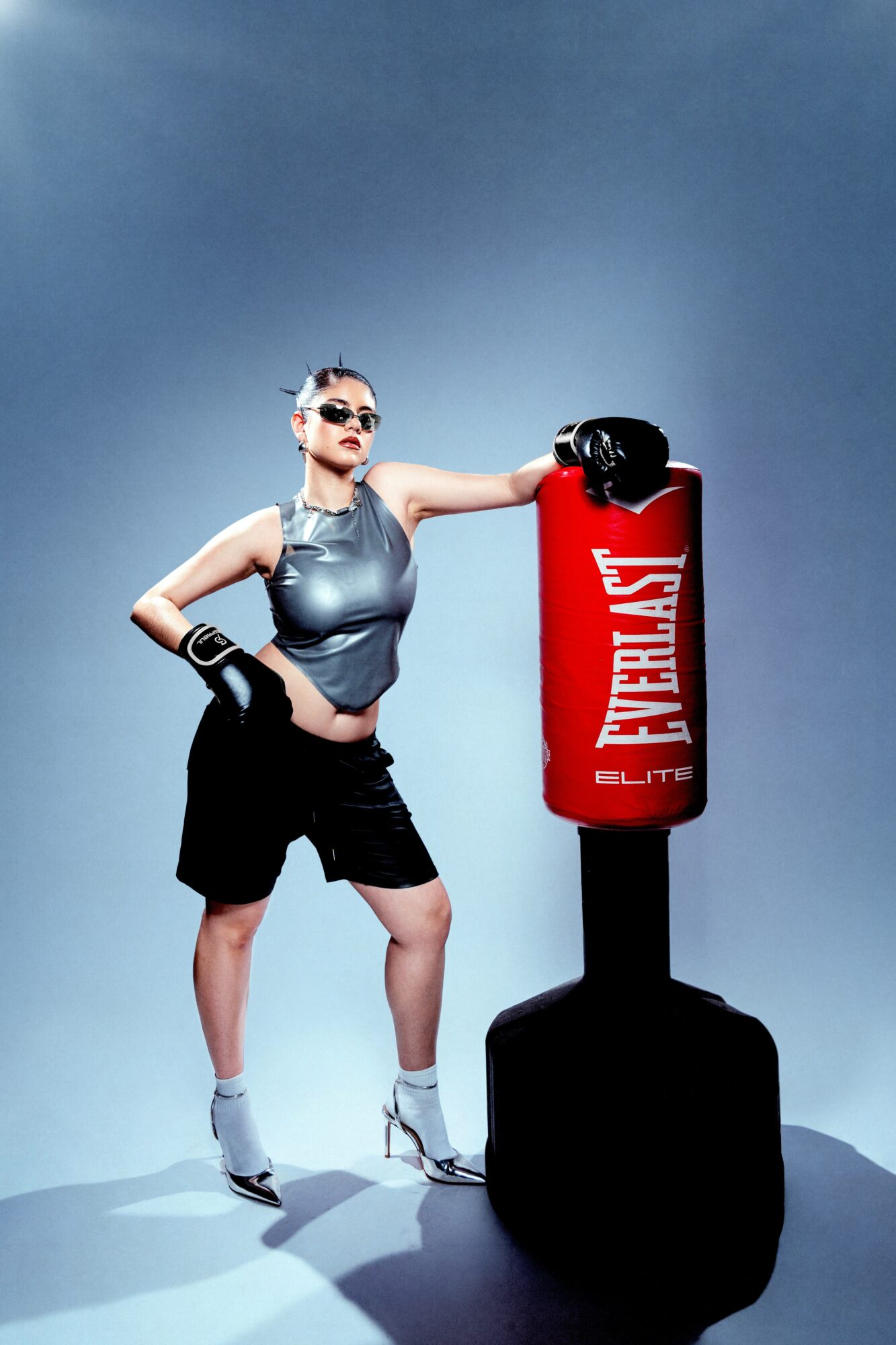 Woman in athletic outfit with boxing gloves standing next to a red punching bag, posing confidently.