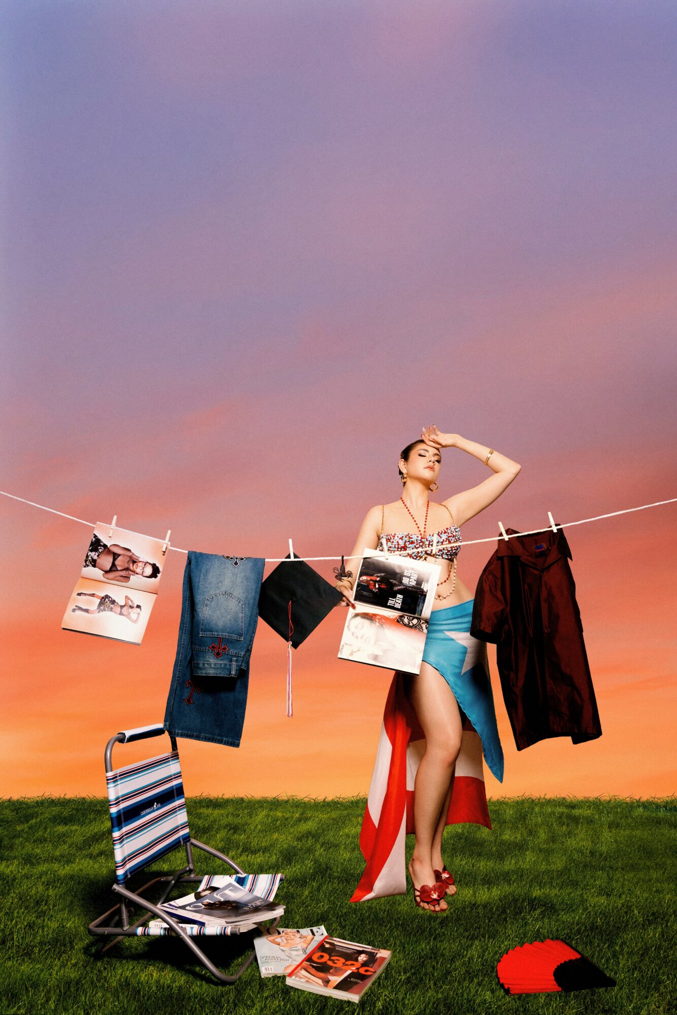 Woman hanging clothes on a line during sunset, with a chair and magazines on the ground.
