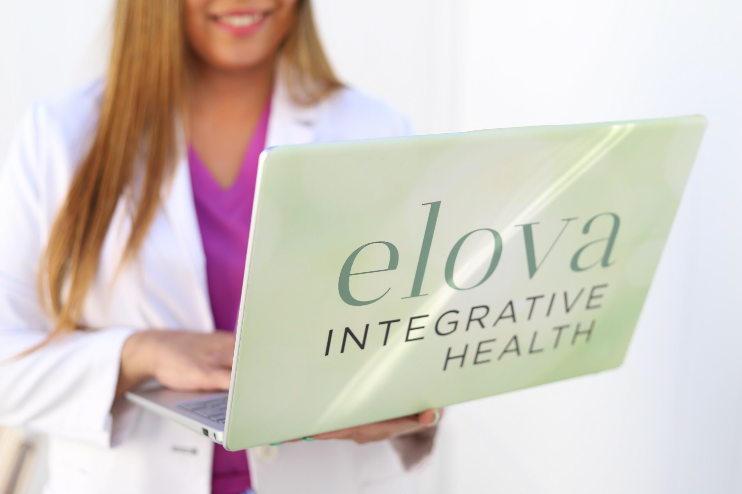 Person holding a laptop with 'elova INTEGRATIVE HEALTH' written on the screen.