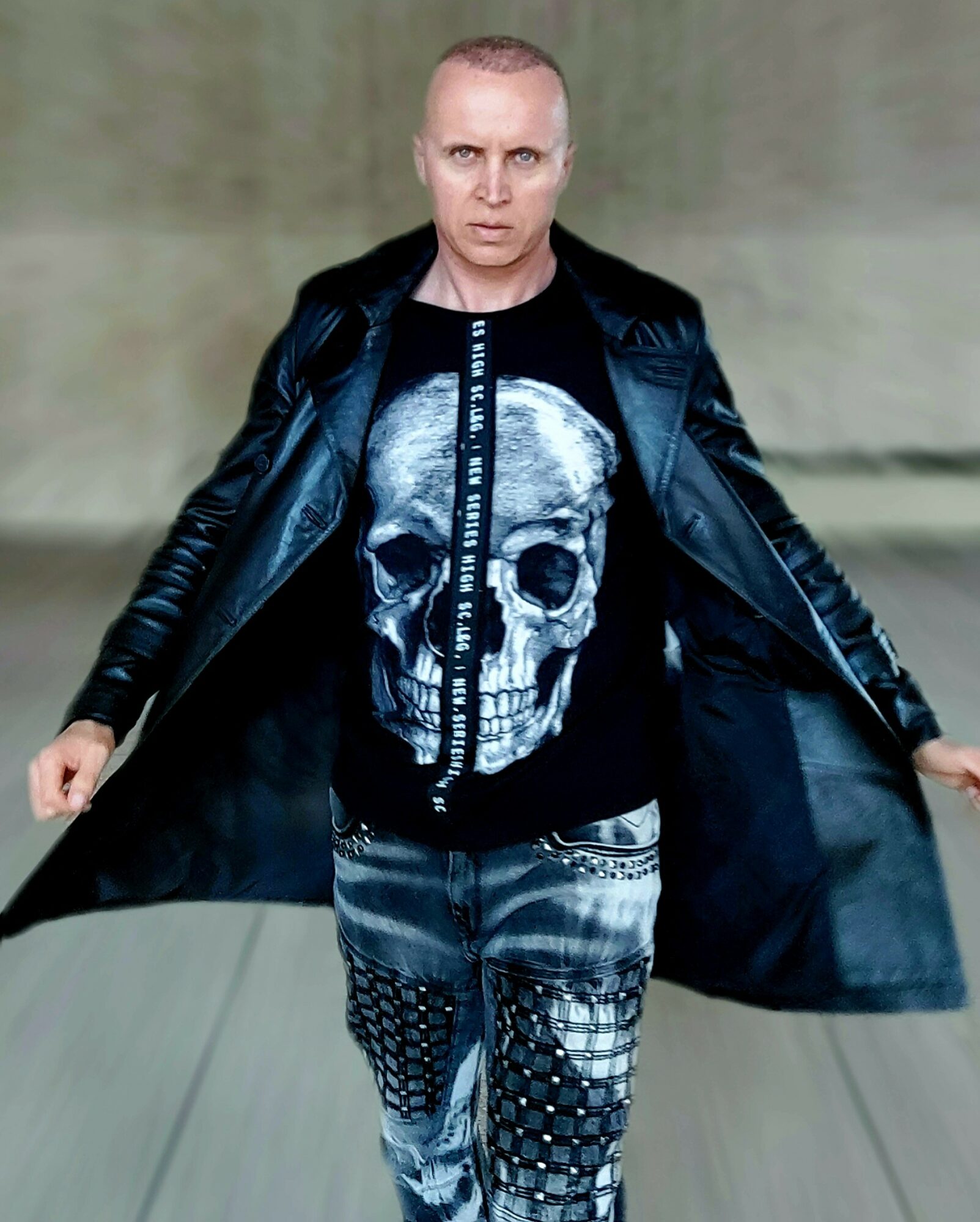 Person with short hair wearing a black leather jacket and a skull graphic shirt, standing indoors.