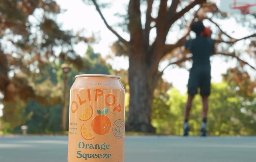 Can with orange and blue design in foreground, person in background hanging from tree branch.